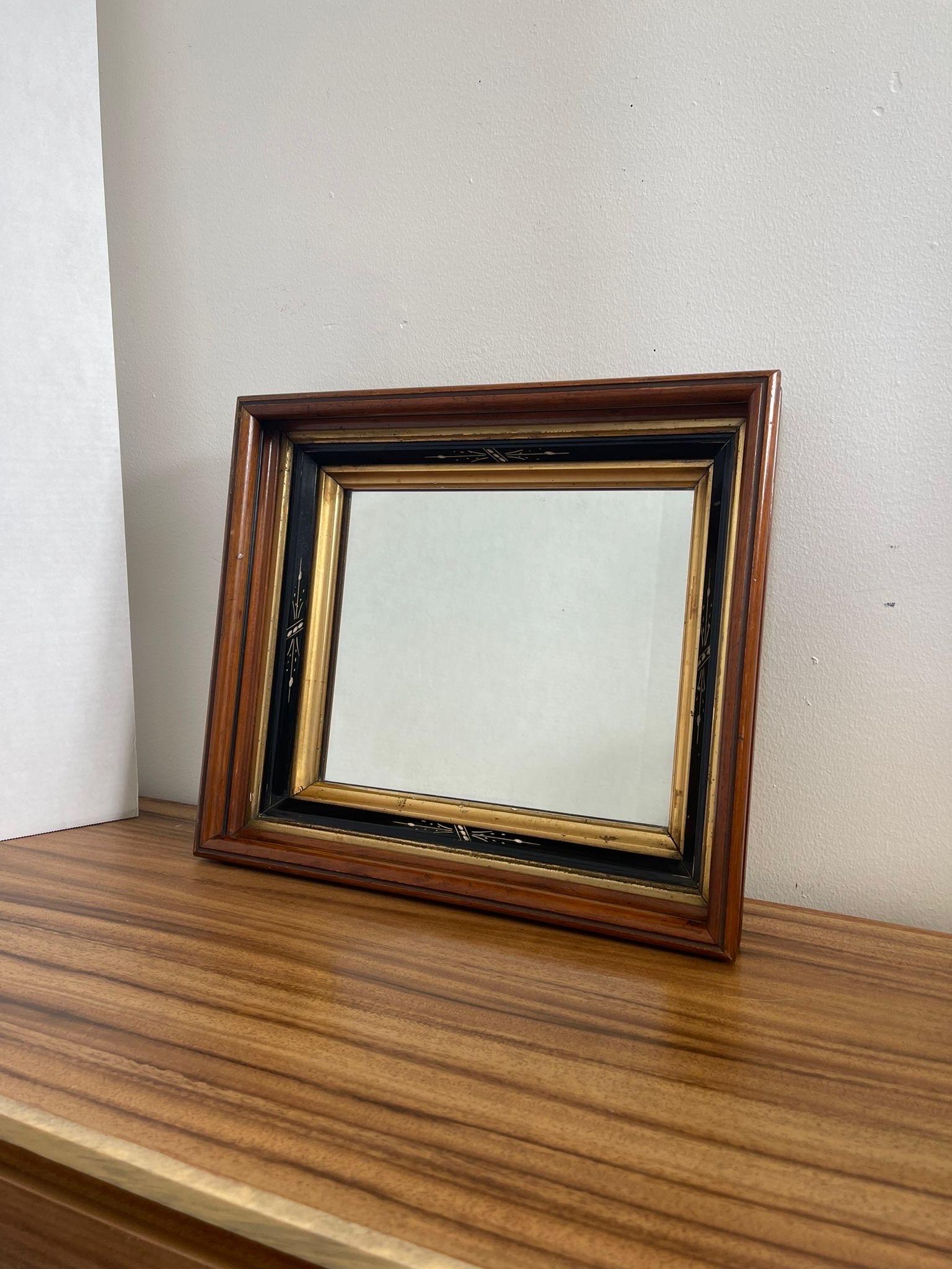 Walnut Toned wood Mirror with painted black and gilt accents. Motif accents each side of the frame. Slight Patina to the glass. Deep set bevel framing. Vintage Condition Consistent with Age as Pictured.

Dimensions. 16 1/2 W ; 3 1/2 D ; 14 1/2 H