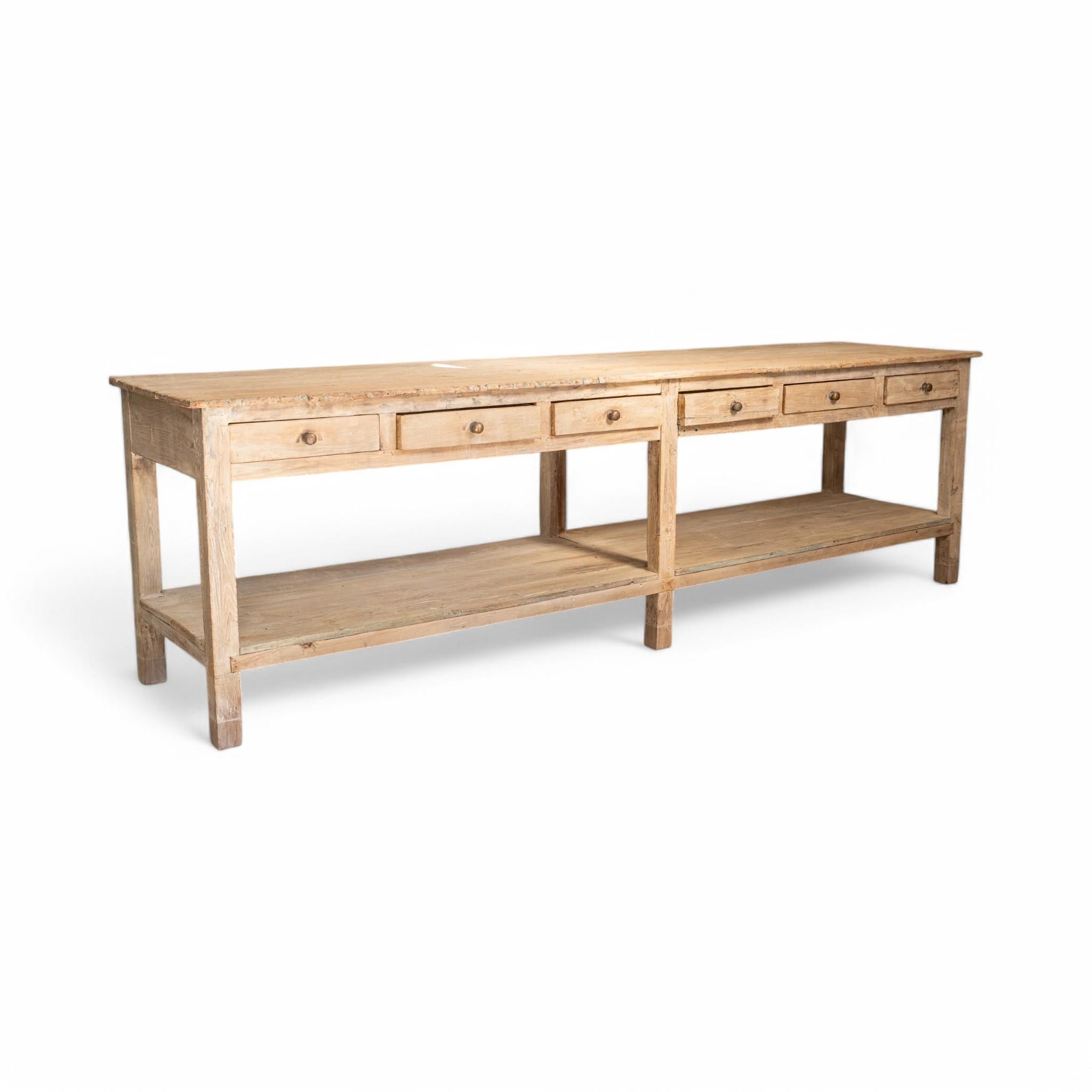 A stunning vintage wood island with a naturally weathered finish, featuring six drawers for storage and a lower shelf for open display. Its generous length and rustic charm make it a versatile piece, perfect as a kitchen island, console, or