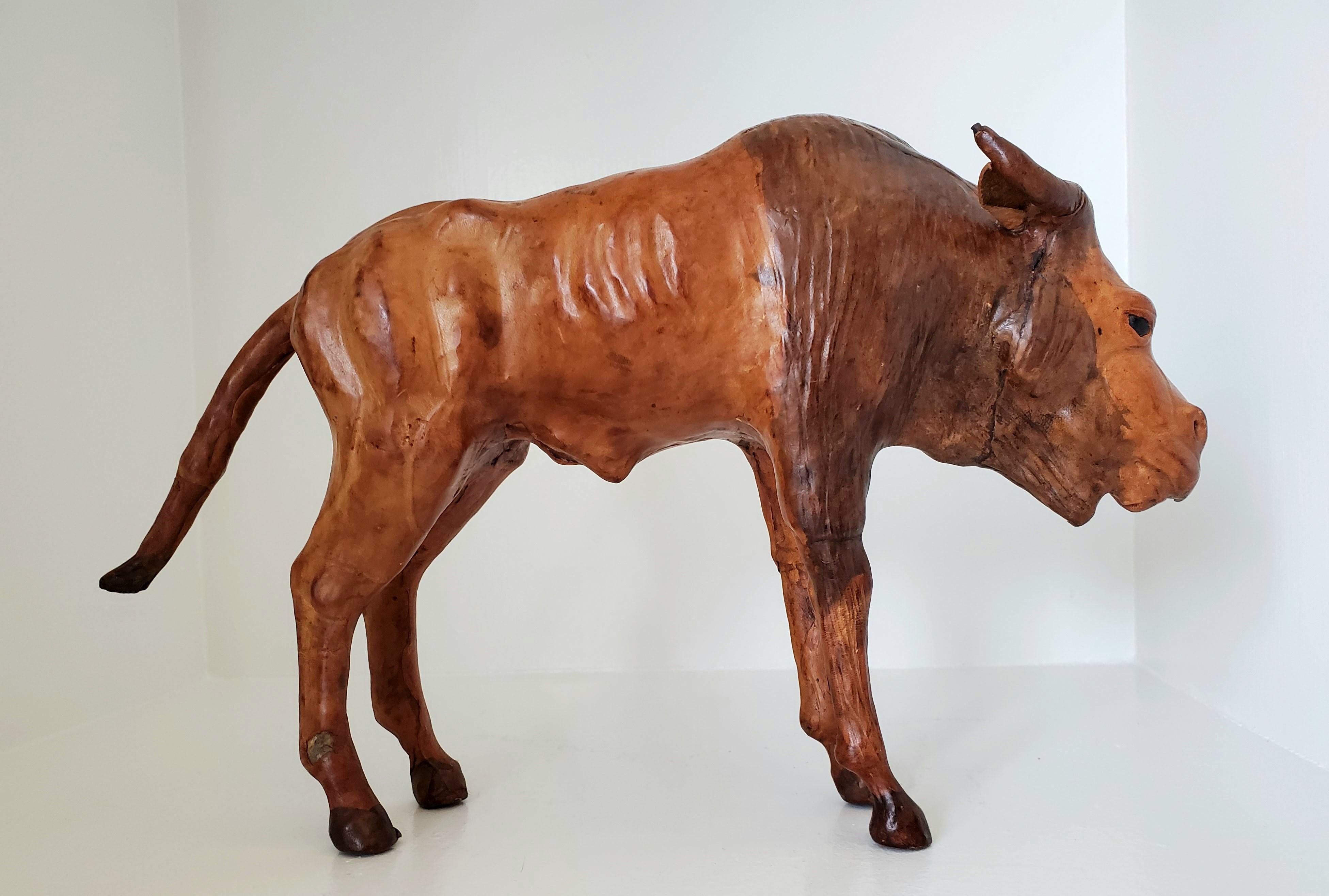This vintage wood and leather animal sculpture from the early 20th century is likely from Liberty's London. This sculpture, handcarved in wood and clad in leather, depicts a lifelike wildebeest that exudes a sense of dolefulness and is realistic in