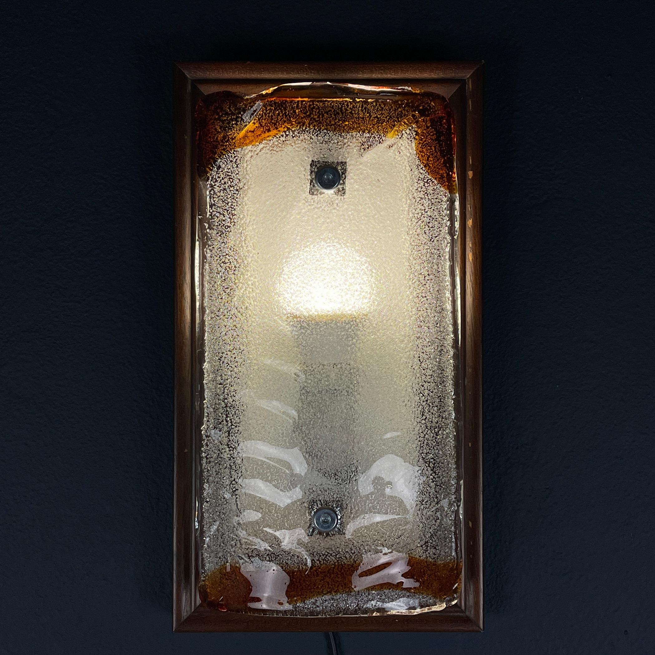 Eleva il tuo spazio con il fascino senza tempo di questa lampada da parete vintage di Murano, una splendida incarnazione del design italiano del Mid-Century Modern degli anni '70. Questa applique vanta un'accattivante cornice in legno che trasmette
