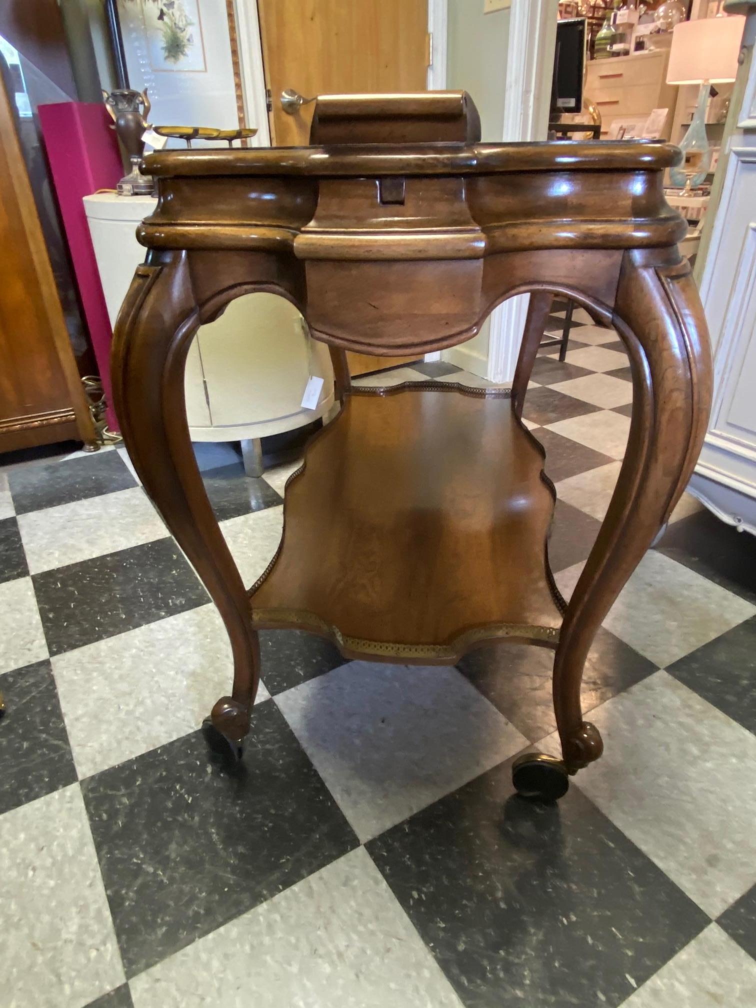 Interesting solid wood bar cart with a brass gallery around the perimeter of the bottom shelf. Curved legs with graceful lines this cart can blend into any decor. The top slides open to reveal a black surface which is water proof and perfect for
