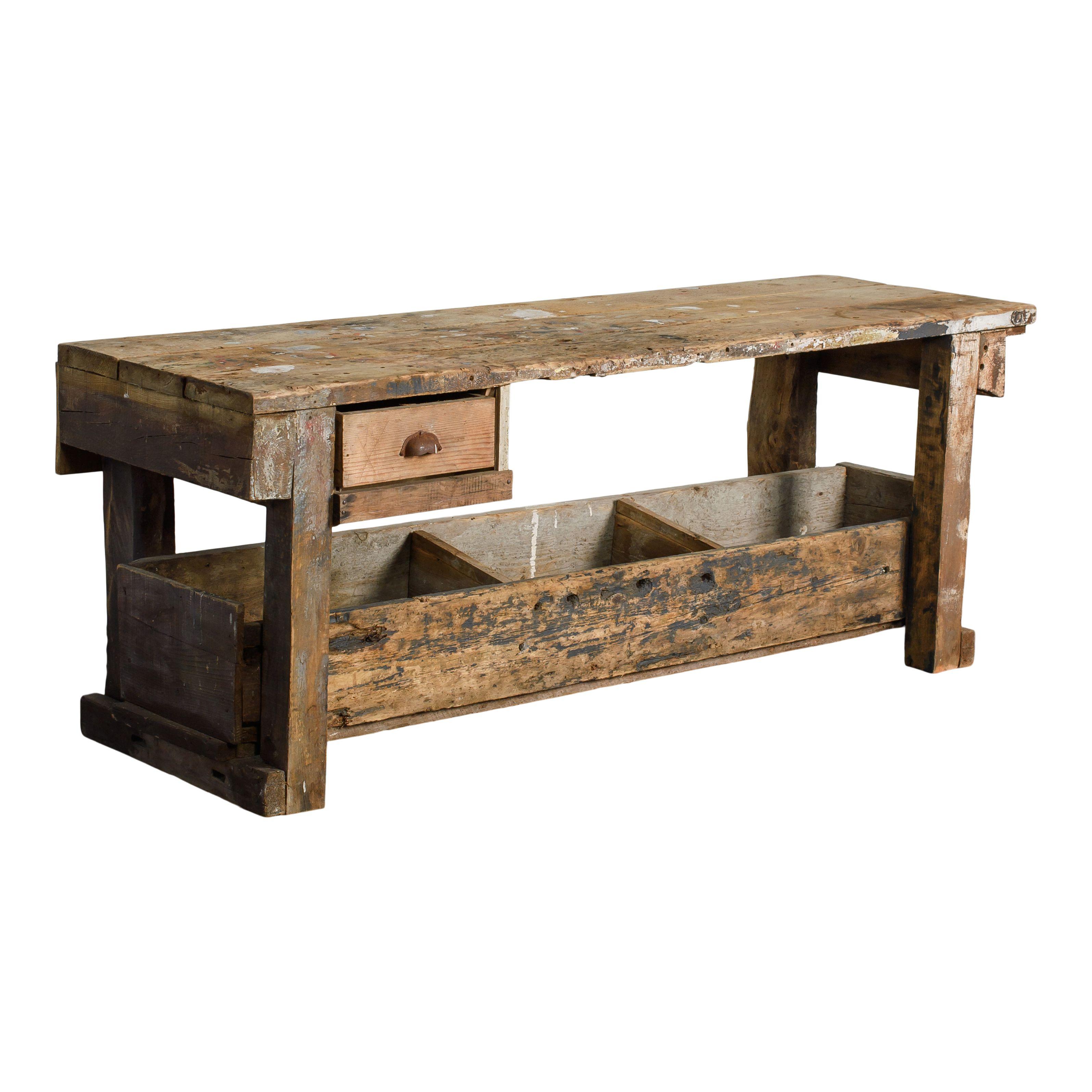 A beautiful vintage wood workbench with a drawer and shelves. This workbench is simple in its design, featuring a tabletop, a small drawer, and open shelves at the bottom. The simple design is enhanced by the signs of wear and use over the years,