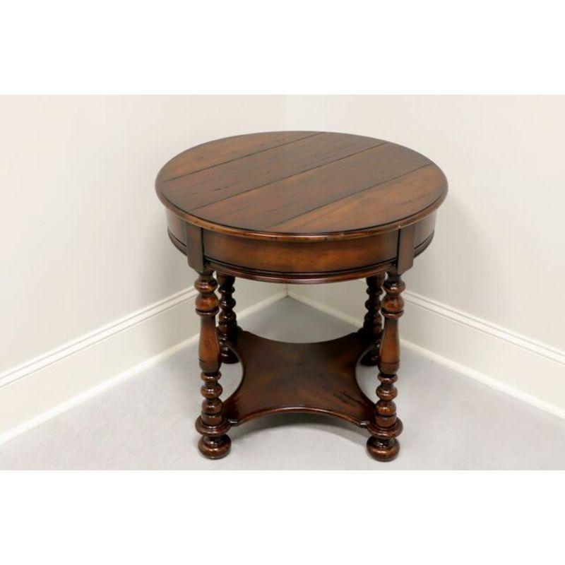 A Rustic style round accent table by Woodbridge Furniture, their Bristol model. Distressed wood with dark stained finish. Features plank style top raised by turned corner posts joined by a lower shelf and bun feet. Made in Asia, in the early 21st