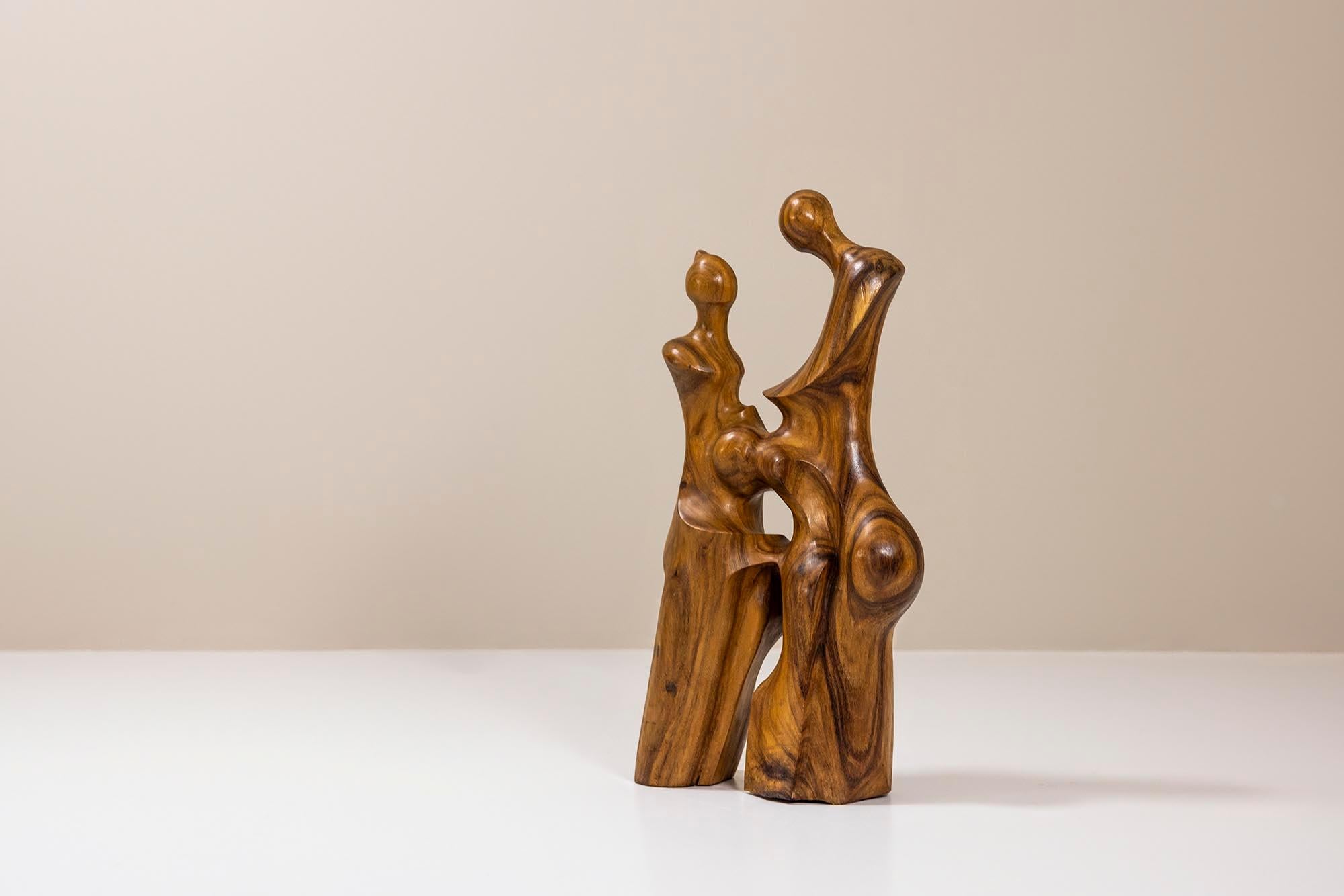 Diese biomorphe balinesische Skulptur aus Nussbaumholz zeigt zwei eng beieinander stehende abstrakte Figuren, die mit fließenden Linien und abgerundeten Formen geschnitzt sind. Die warmen Töne der natürlichen Maserung des Walnussholzes heben die