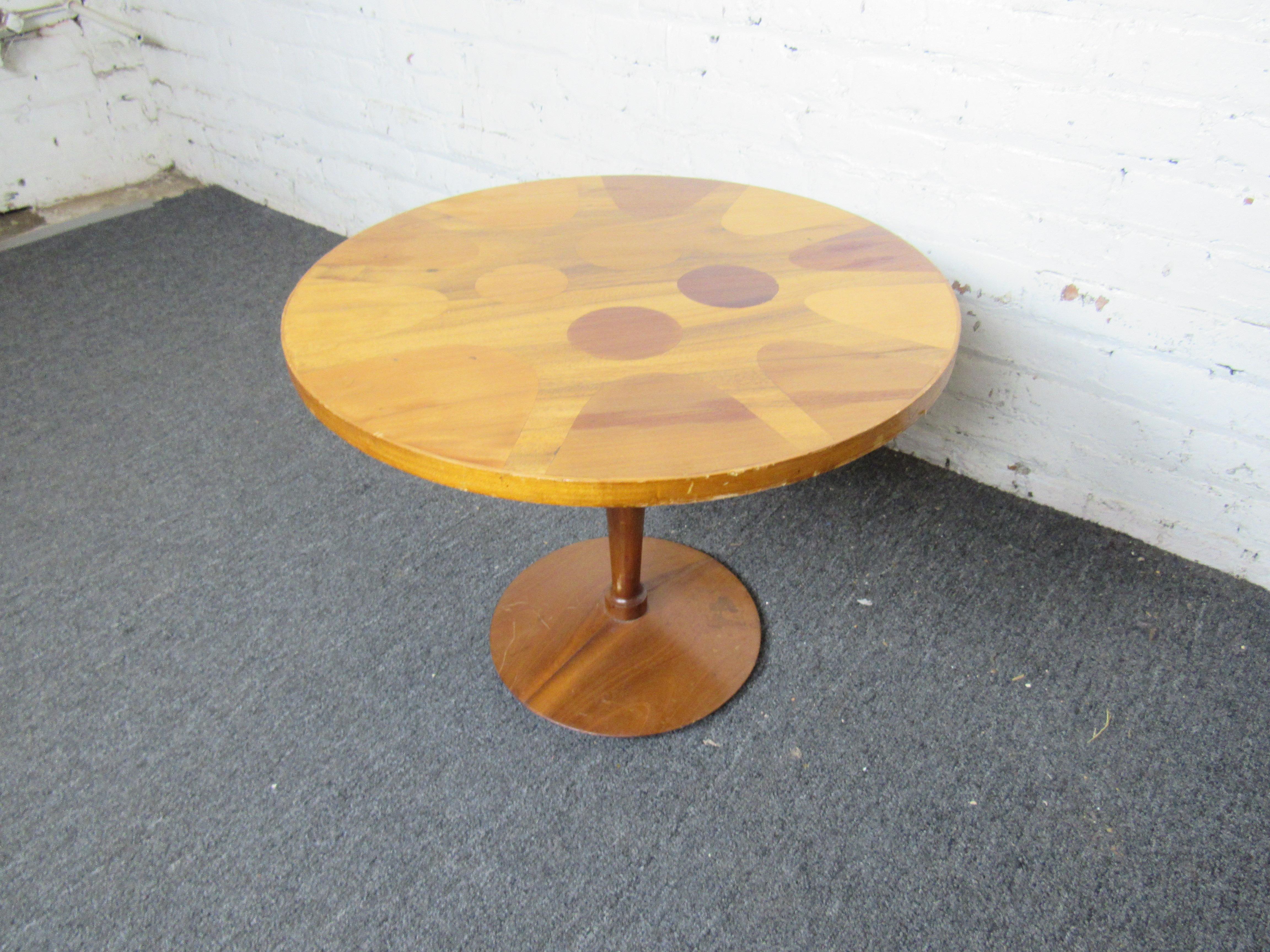 This interesting vintage table is perfect for enjoying a cocktail or coffee with guests. Featuring a circular design using different shades of stained wood as well as a sleek sculpted base, this table is sure to make an eye-catching addition to any