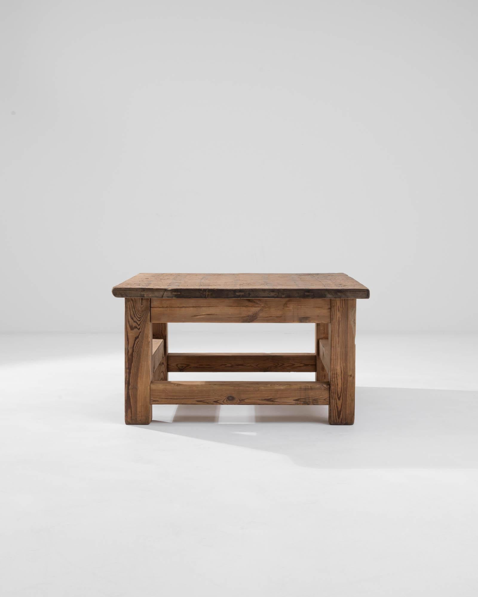 This vintage wooden coffee table, made in Central Europe, showcases an understated silhouette punctuated by its flat tabletop, sturdy square legs, and the interplay of side stretchers built at different levels, creating an asymmetric effect. The