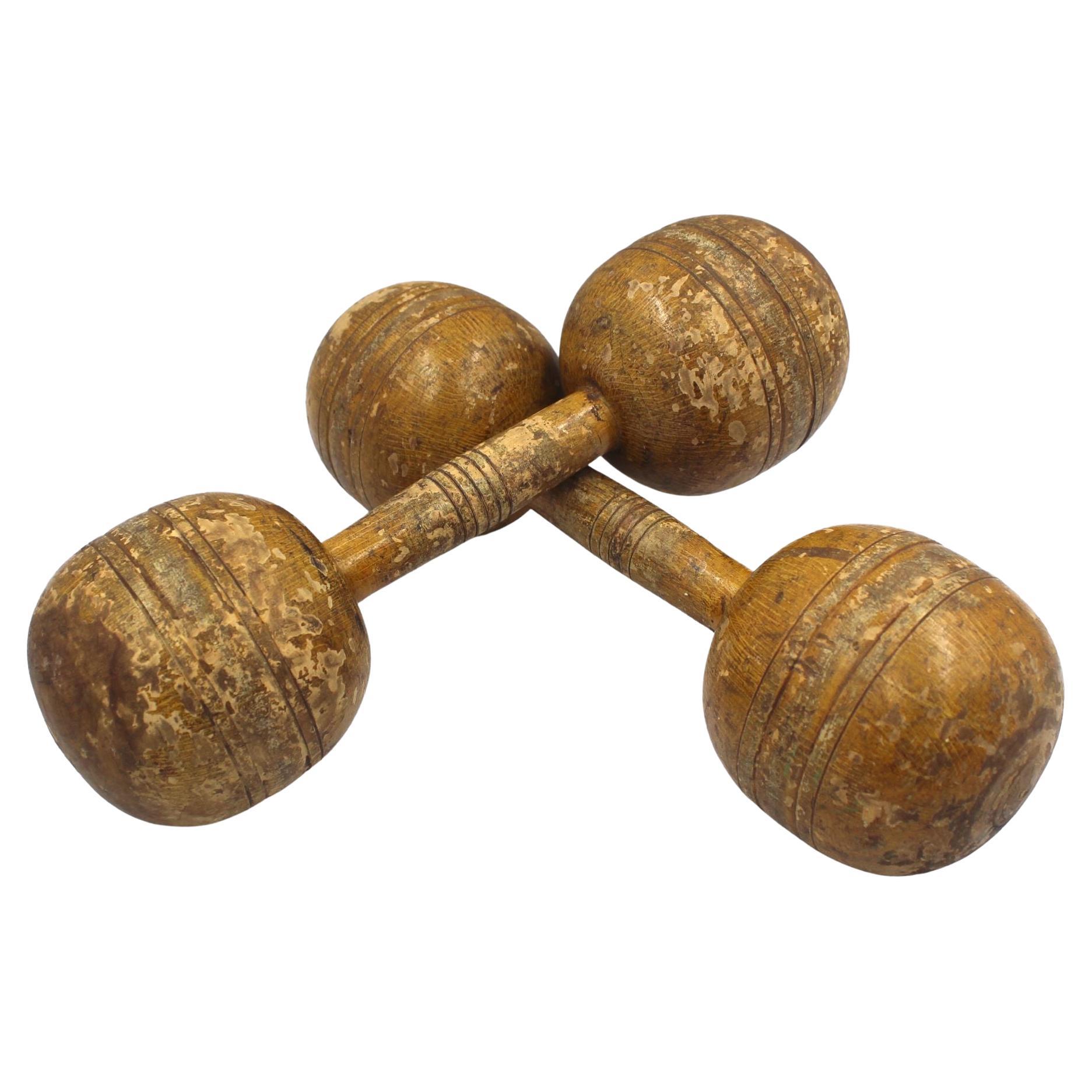 Presented is a set of vintage wooden dumbbells. The dumbbells are fixed-weight and constructed of hand-turned solid wood. They have incised lines at center for grip and around the balls for ornamentation and to keep the dumbbells from rolling. A