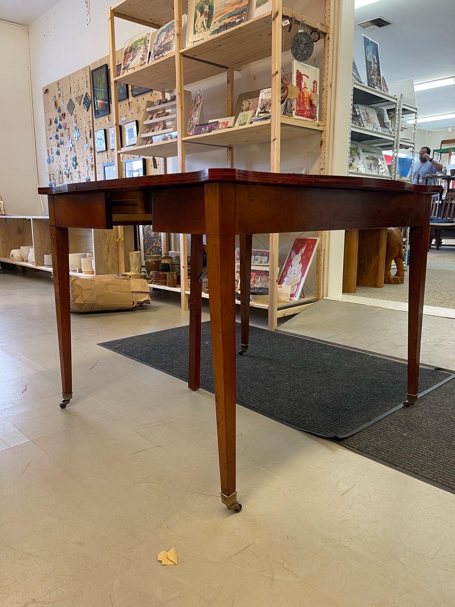 This extending table can be used as a Console Table or Dining Table. The extra leg in the center provides stability and durability. Beautiful floral wood inlay detailing accents the front of the piece. Black lining details the edge of the piece.The