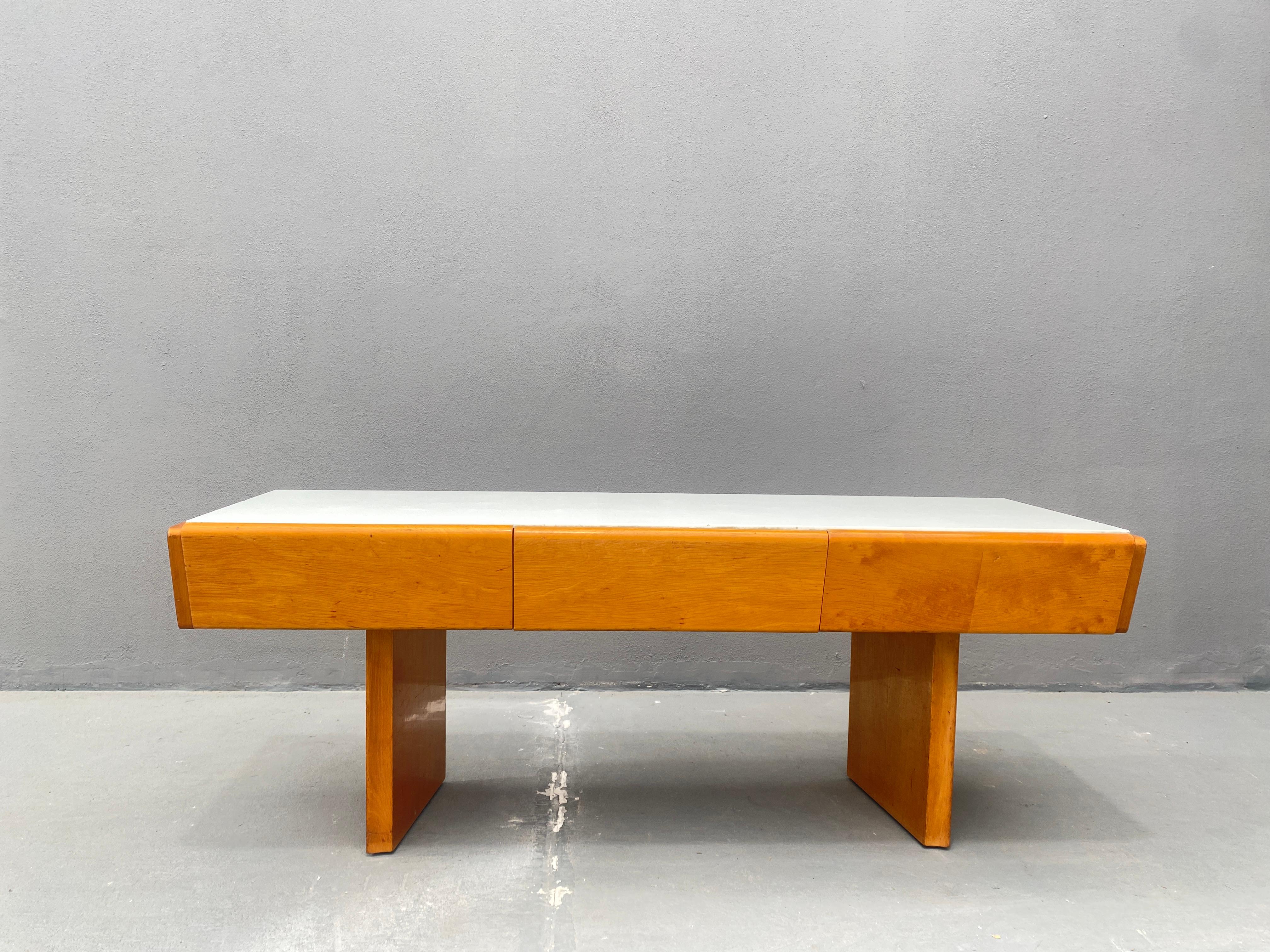 Esta consola baja vintage tiene su origen en la década de 1960. Es de madera, con tapa de cristal opalino blanco. El mueble está diseñado con tres cajones frontales, que proporcionan espacio de almacenamiento. La consola permanece en su estado
