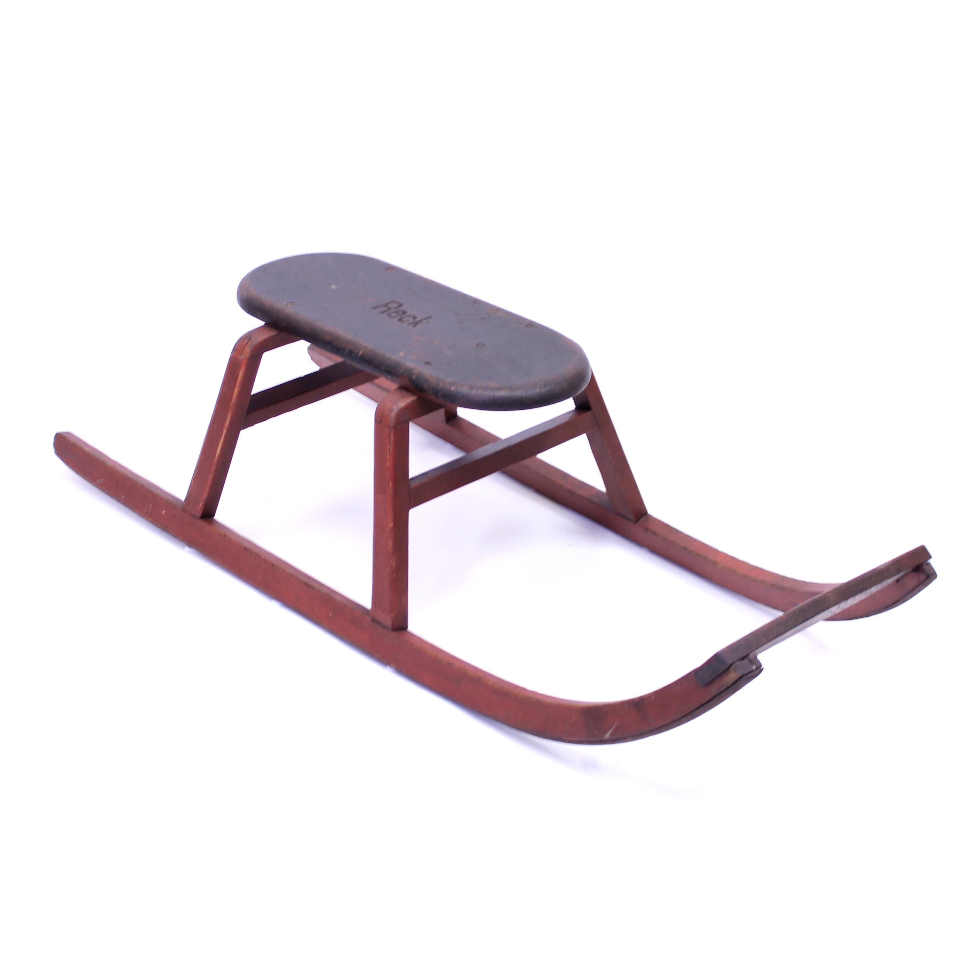 Wooden sled with metal runners under the rockers. The legs and rockers have the original red paint and the seat has its original dark stained wood with very honest and attractive patina from years of use. The seat is marked RECK. It contains normal
