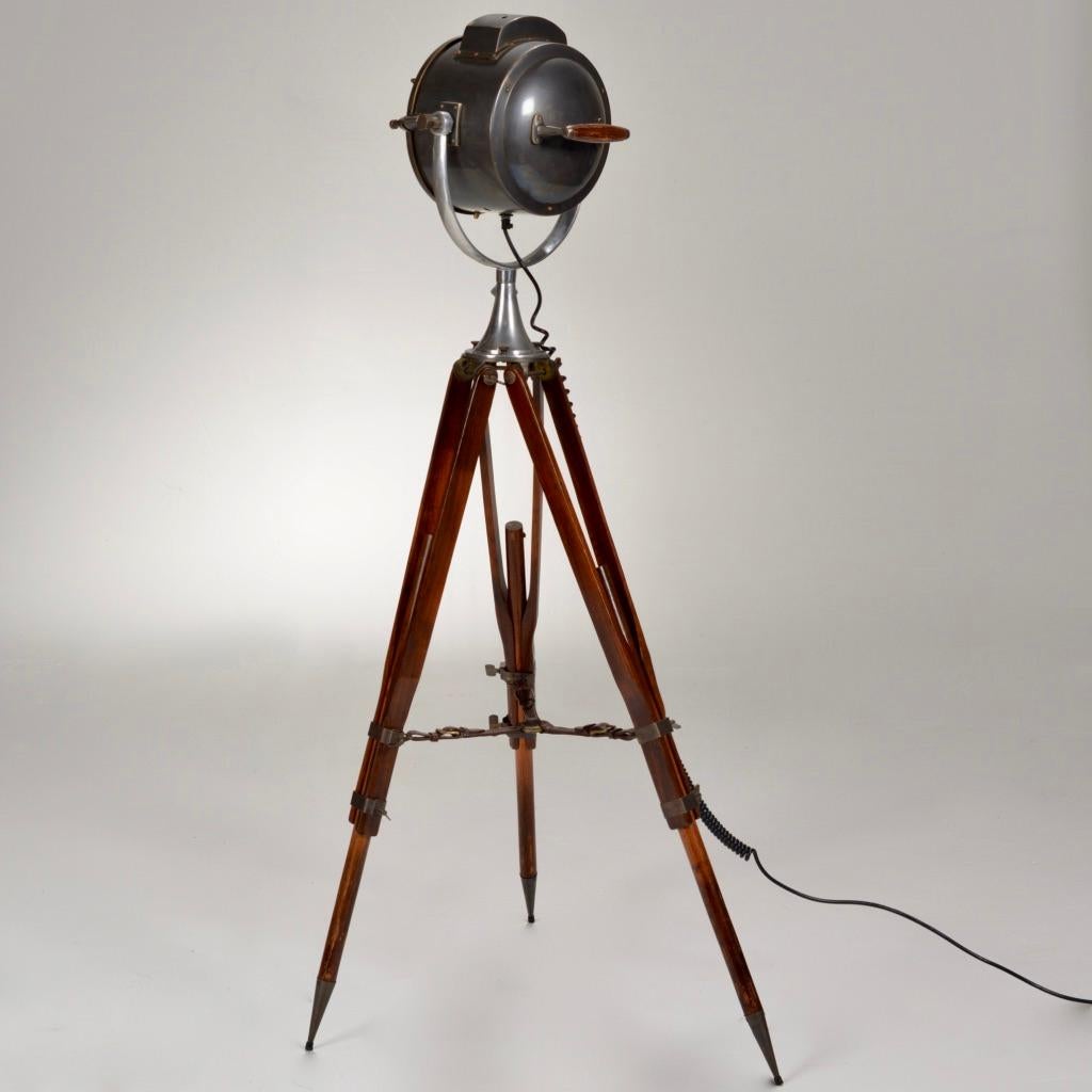 Tripod floor lamp with wooden legs and a brass body. This lamp features a wooden handle on the back on the adjustable body for easy movement with knobs to tighten the placement. The height of the legs can be adjusted as well. In addition, the