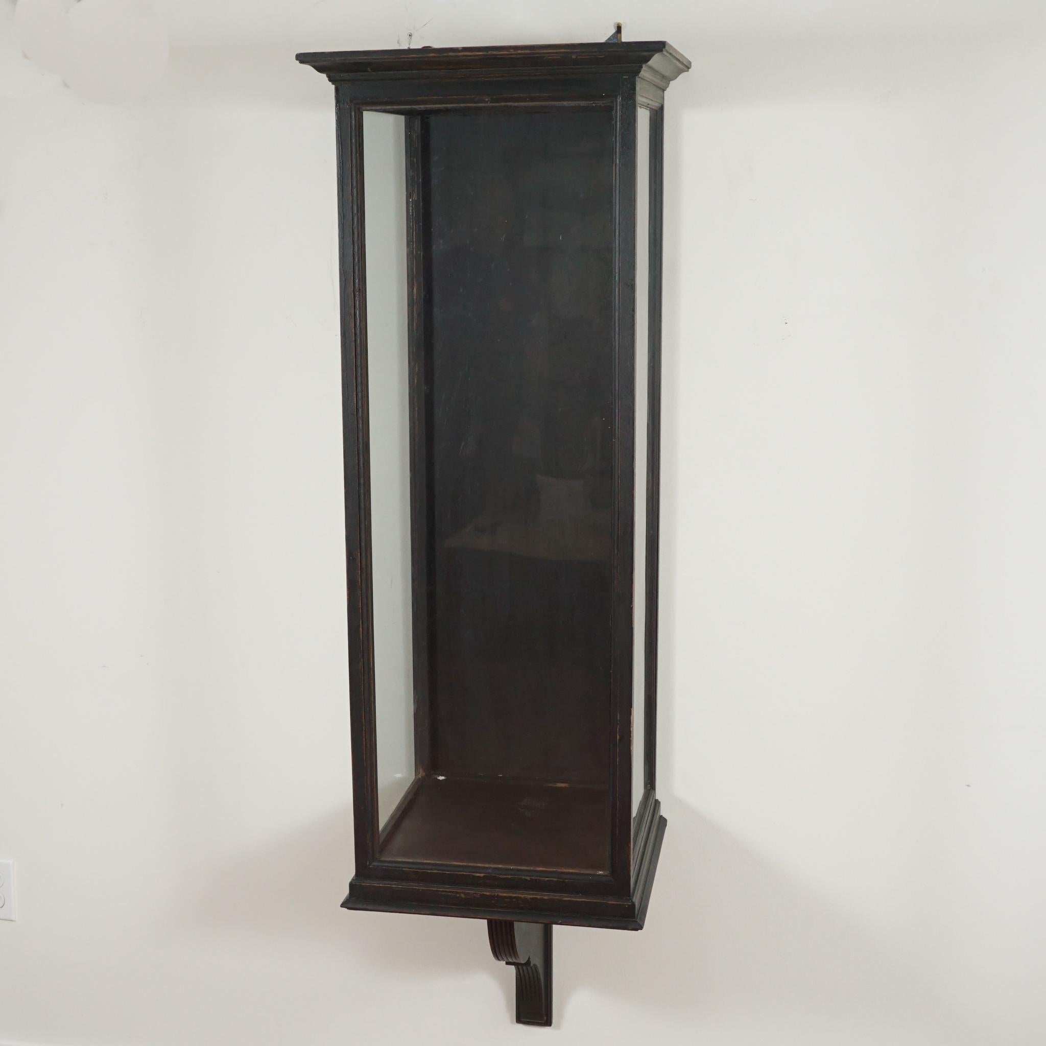 The scale and design of this 1920s wall-mounted wood vitrine is certain to add decorative interest to any interior.   Featuring a slightly distressed wood finish and seeded glass, the interior is easily accessed through the top.   One-of-a-kind from