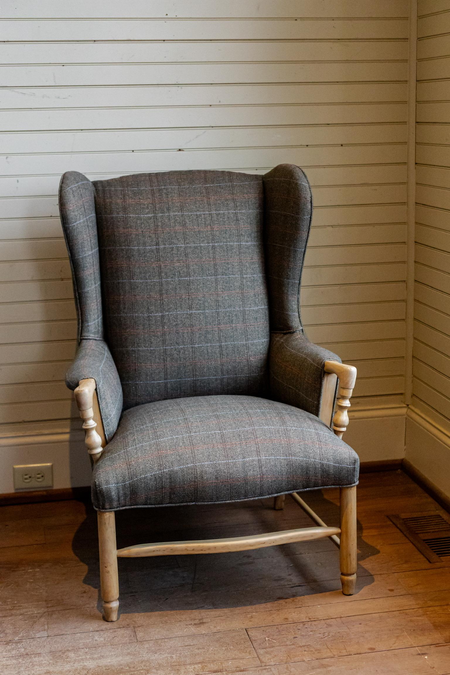 Sillón danés vintage con respaldo vuelto, retapizado con tela escocesa de lana marrón de diseño y bonitos brazos y patas de madera vista en tonos naturales.