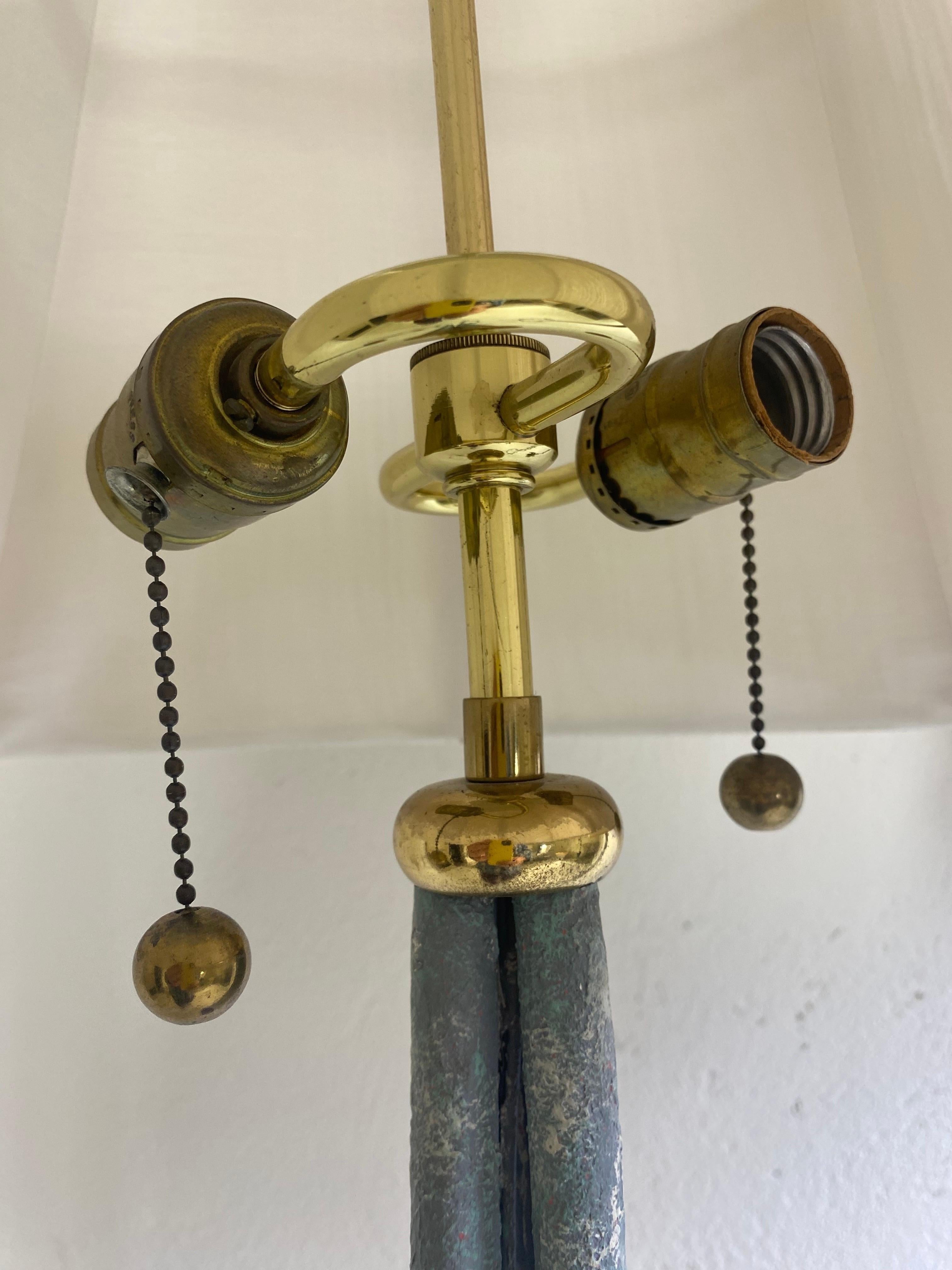 This is a pair of 20th century vintage hand wrought iron floor lamps. This pair of floor lamps are topped with solid brass S cluster sockets and fittings mounted at the top. The iron bases have a distressed oxidized finish to the surface and have a