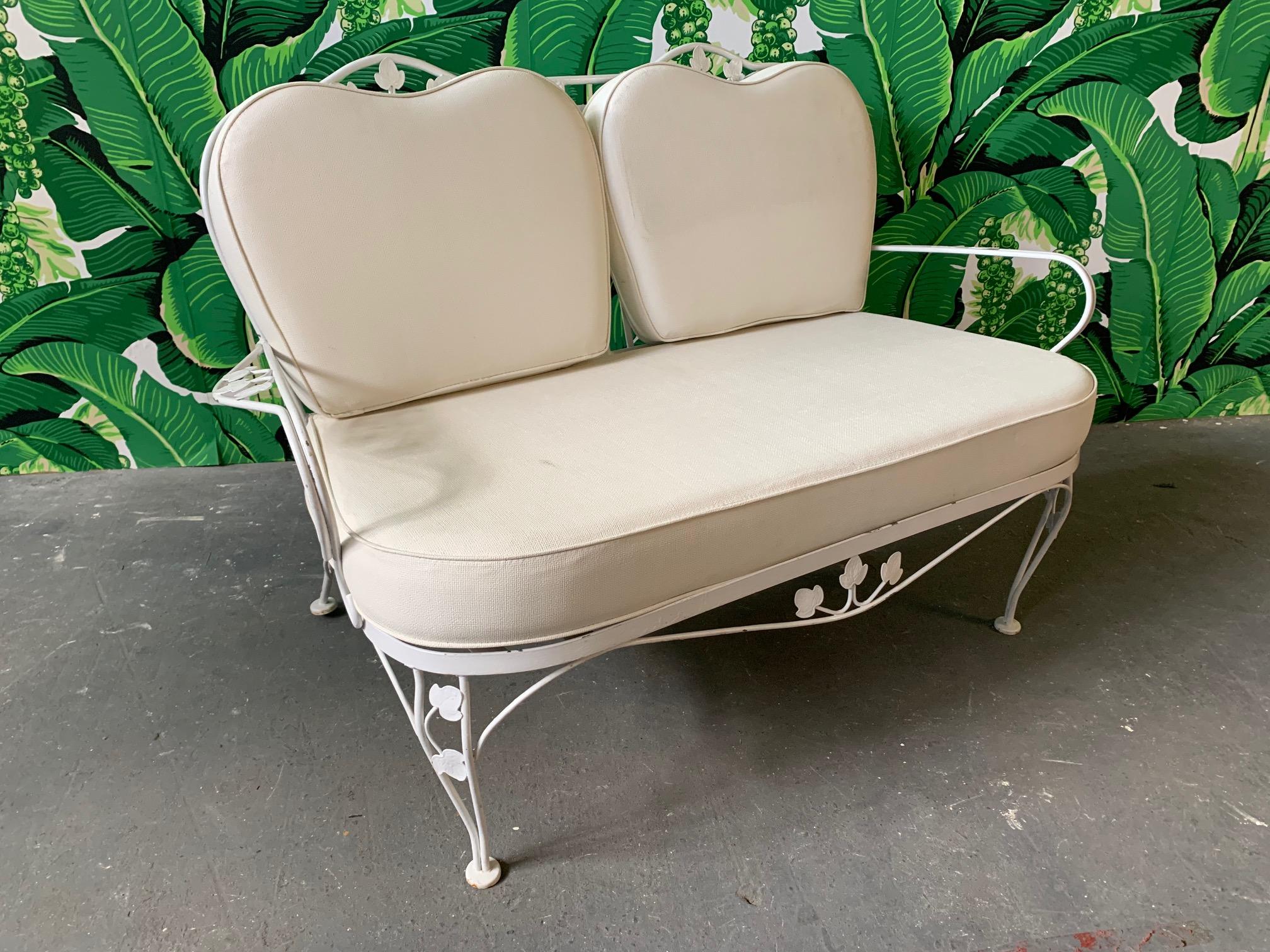 Vintage wrought iron loveseat by Lee Woodard and Sons (father of Russell Woodard) features decorative ivy detailing and original floral upholstery. Fabric has flaws but white vinyl is in very good condition, cushions can be flipped as in photos.