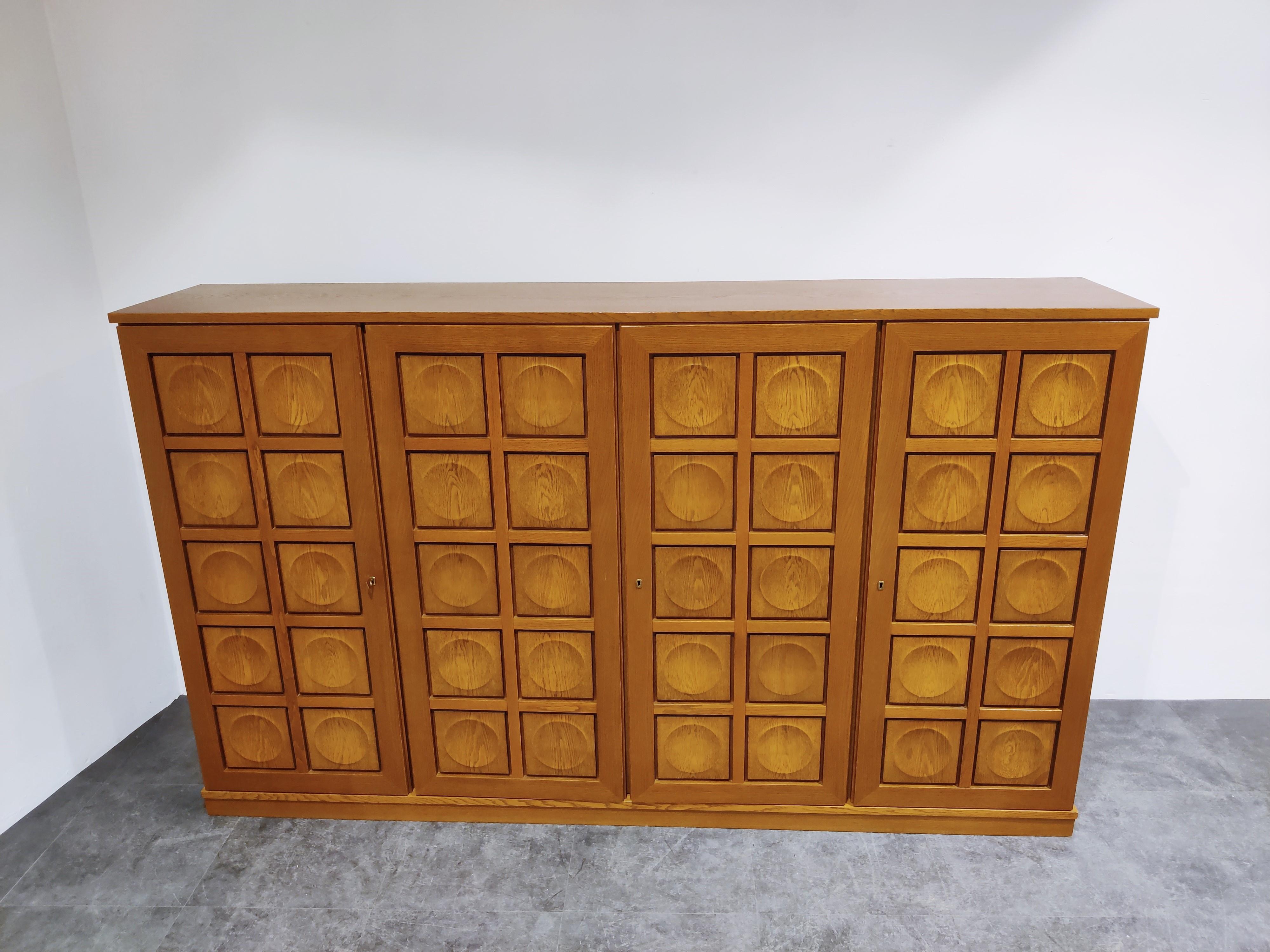 Striking and large Brutalist highboard with graphical door panels.

Made from oak.

Consists of four doors revealing plenty of storage space and two drawers.

Good condition two minor repairs on base corner and top corner.

Manufactured by