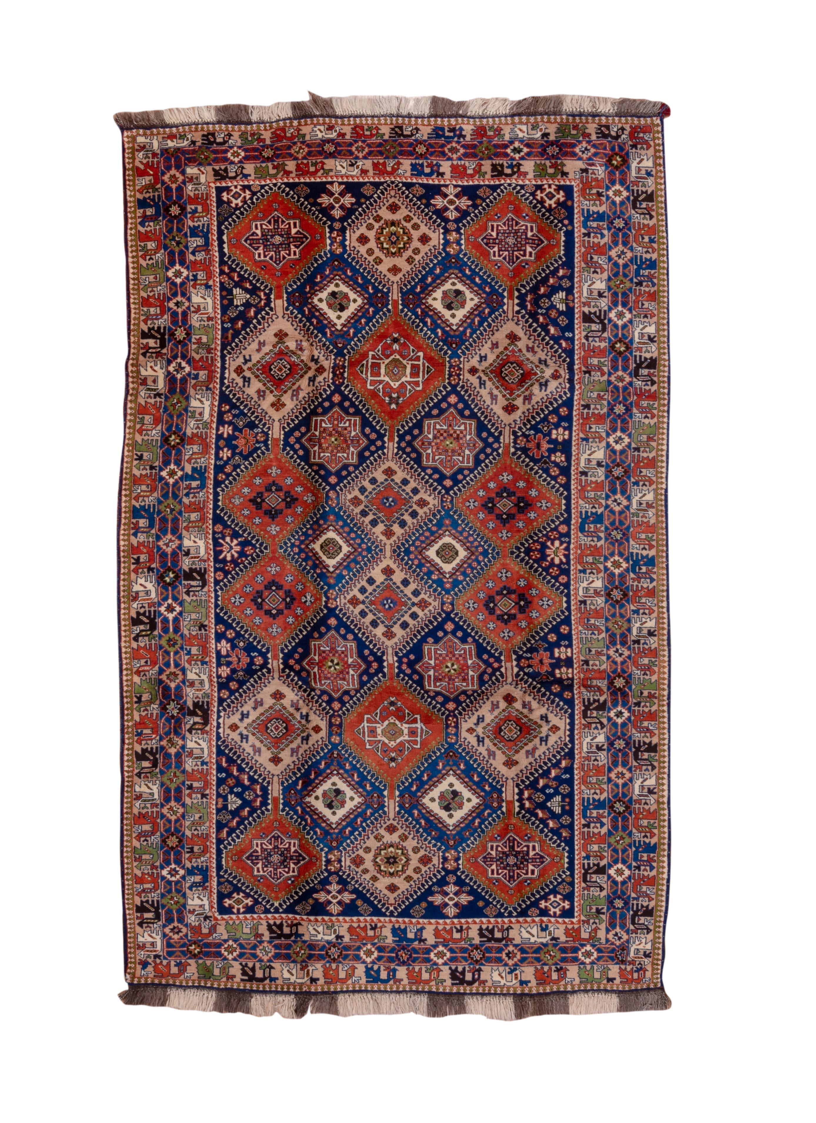 This vintage Yalemeh rug captivates with a symmetrical grid of star medallions in alternating hues of rust, ivory, sapphire, and forest green. Set against a midnight blue field, each lozenge-shaped panel is punctuated with tribal symbols, stylized