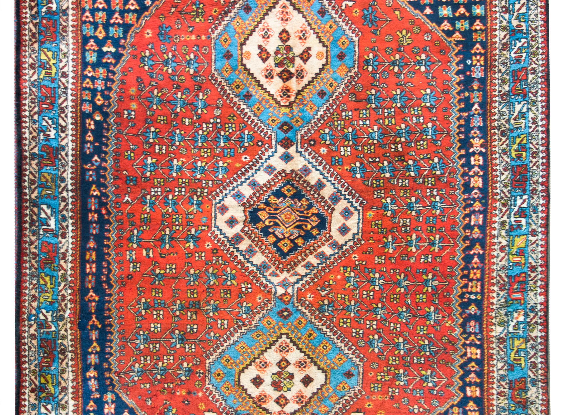 A stunning vintage Persian Yallameh rug with three large central diamond medallions woven with stylized flowers and vines, and living amidst a field of even more densely woven stylized flowers, woven in indigo, gold, white, and crimson, and