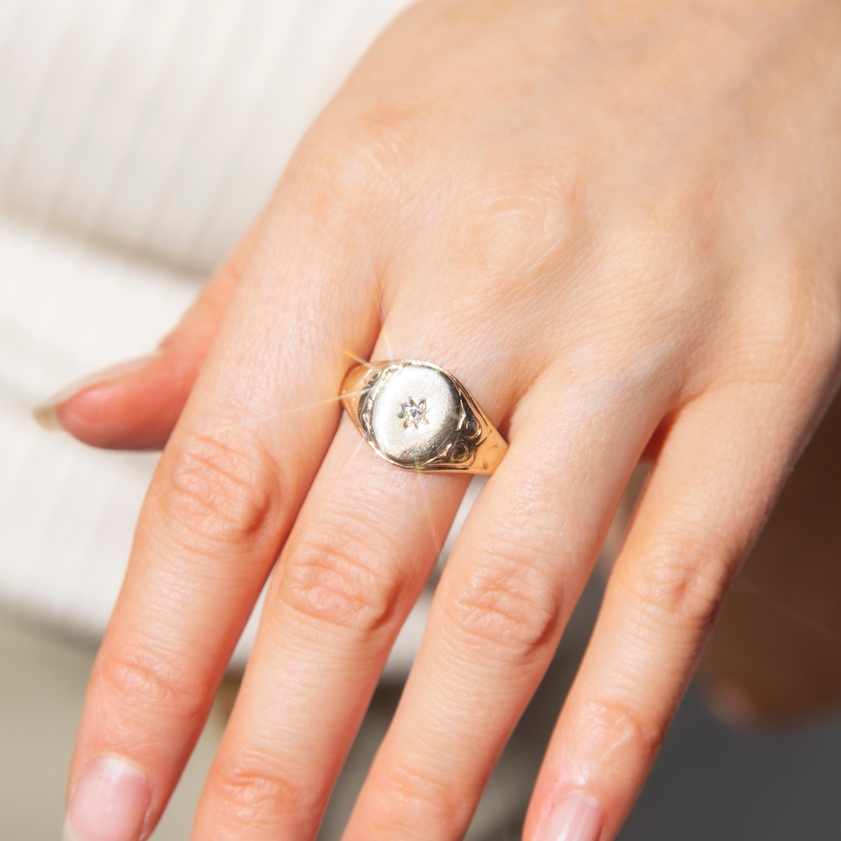 Crafted in 9 carat yellow gold, this lovely vintage signet ring features a high polish band flowing out into patterned shoulders and a round platform with a shimmering hammer set diamond at the centre. We have named her The Romy Ring. She fits low