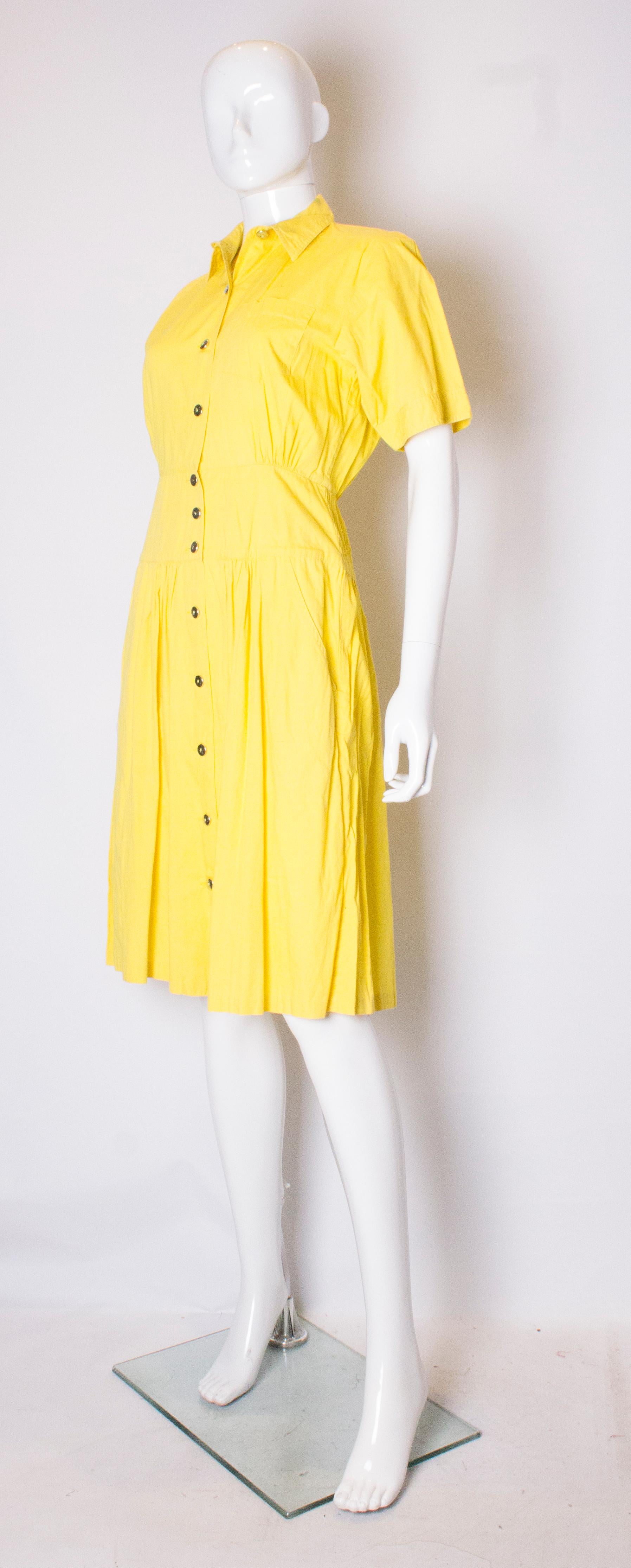 A vintage yellow cotton day dress by Expressions. The dress has a button through front with 12 buttons. It has short sleaves, gathering at the back with one breast pocket and two pockets and hip leval.