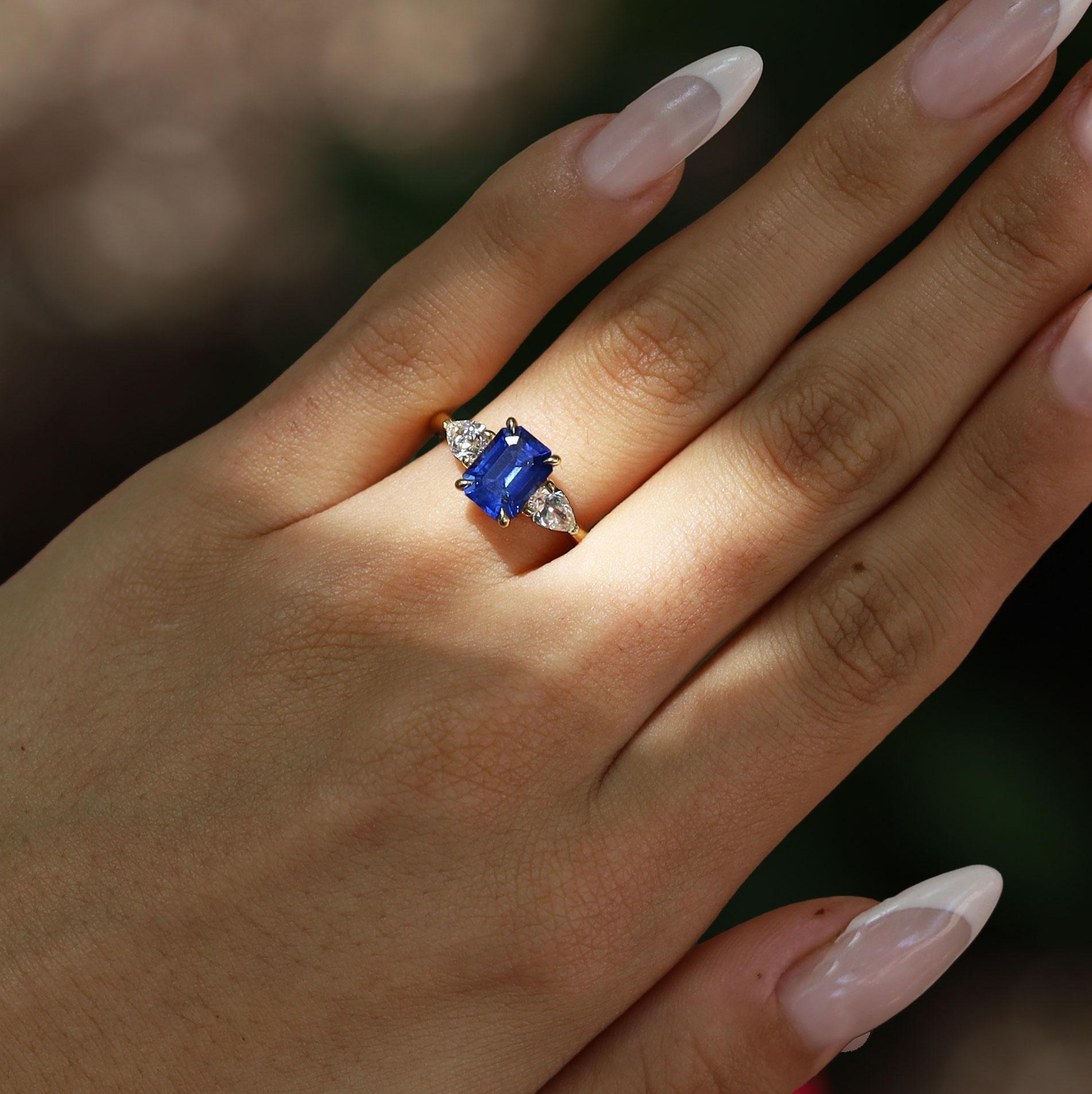 This captivating, vintage 3 stone sapphire engagement ring is centered with a strikingly blue and lustrous sapphire weighing 2.50 carats and set into classic claw prongs. The shoulders of the ring are each accented with a pear shaped diamond,