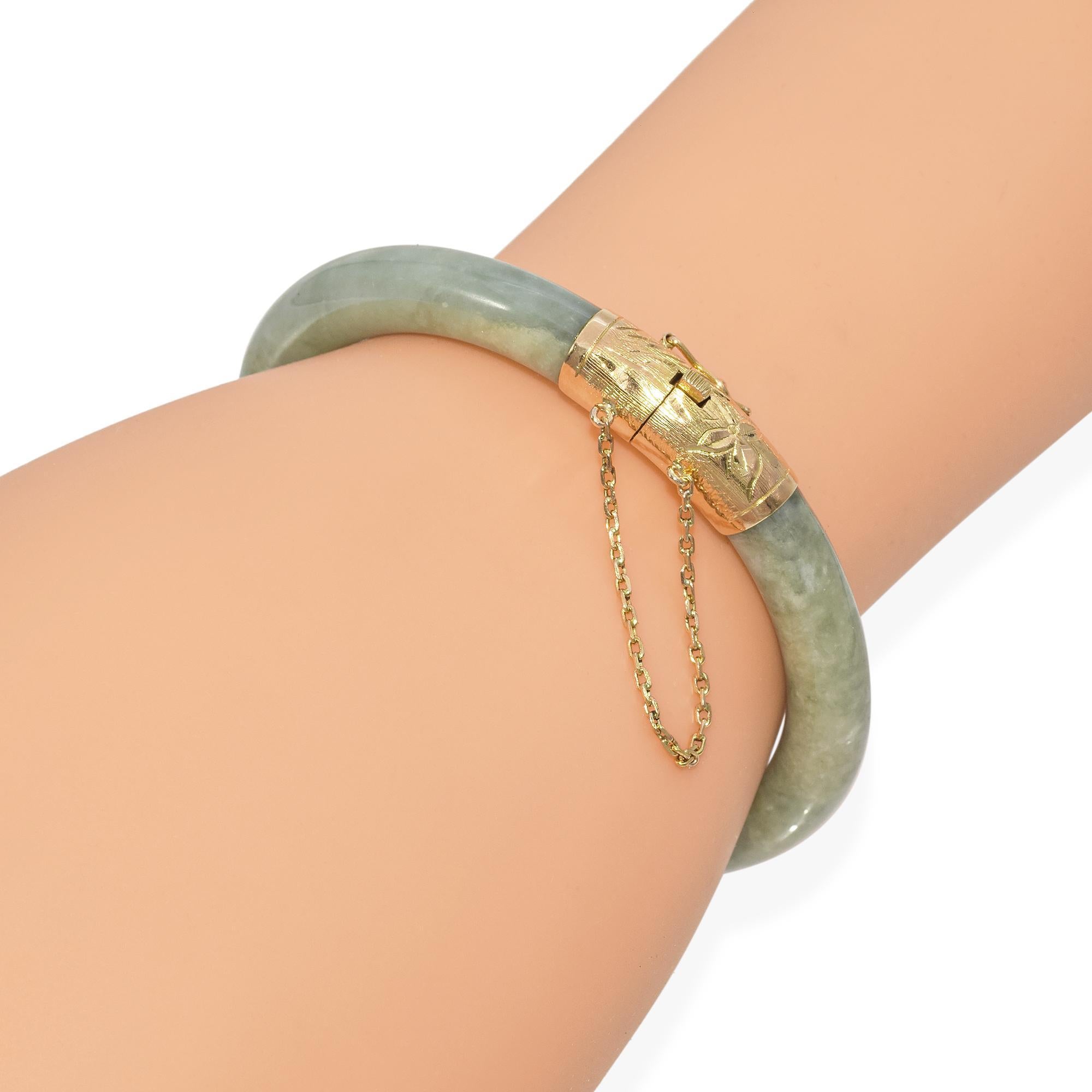 Ein raffinierter Armreif mit einem glatten, grünen Jadeband. Die Jade weist einen ruhigen, natürlichen Farbton auf, der durch den warmen Schimmer von Gelbgoldakzenten noch verstärkt wird. Das Gold ist aufwändig graviert und verleiht dem Design einen