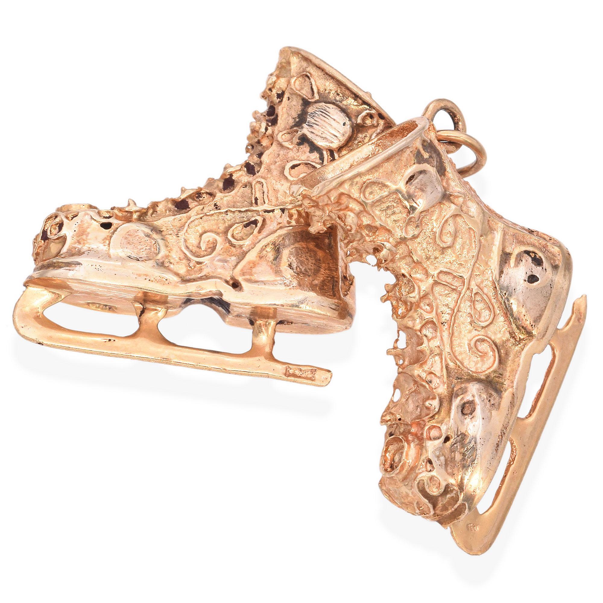 Cette breloque complexe représente une paire de patins à glace, travaillée avec minutie. Les patins sont ornés de motifs tourbillonnants et d'embellissements texturés, ce qui leur confère un aspect unique et orné. Chaque patin est relié par un petit