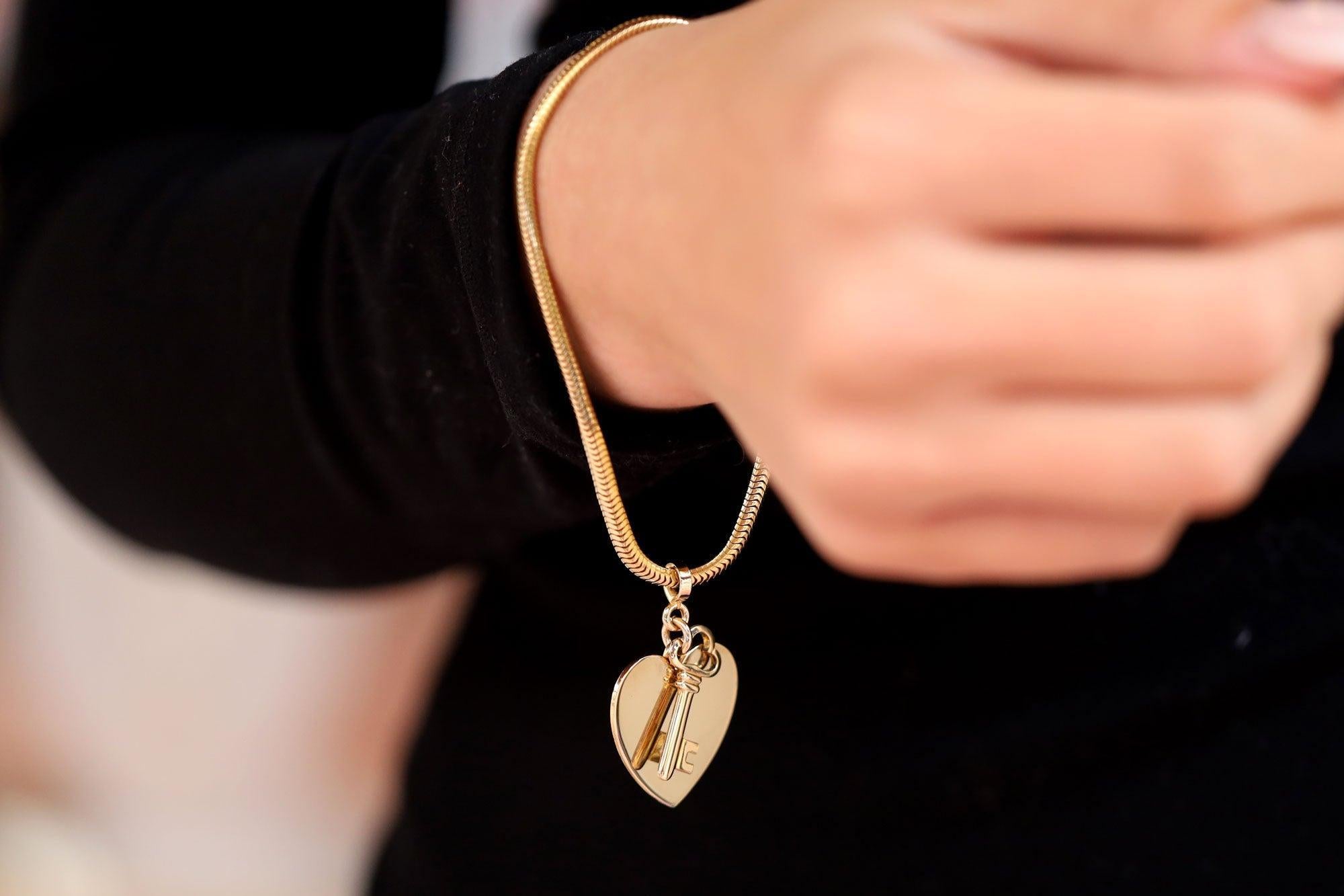 A vintage yellow gold slinky snake bracelet suspending dangling heart and key charms. Similar to the iconic design by Tiffany & Co. circa 1960s. This whimsical bracelet, symbolizing 'Key to My Heart', exudes a nostalgic charm that captures the