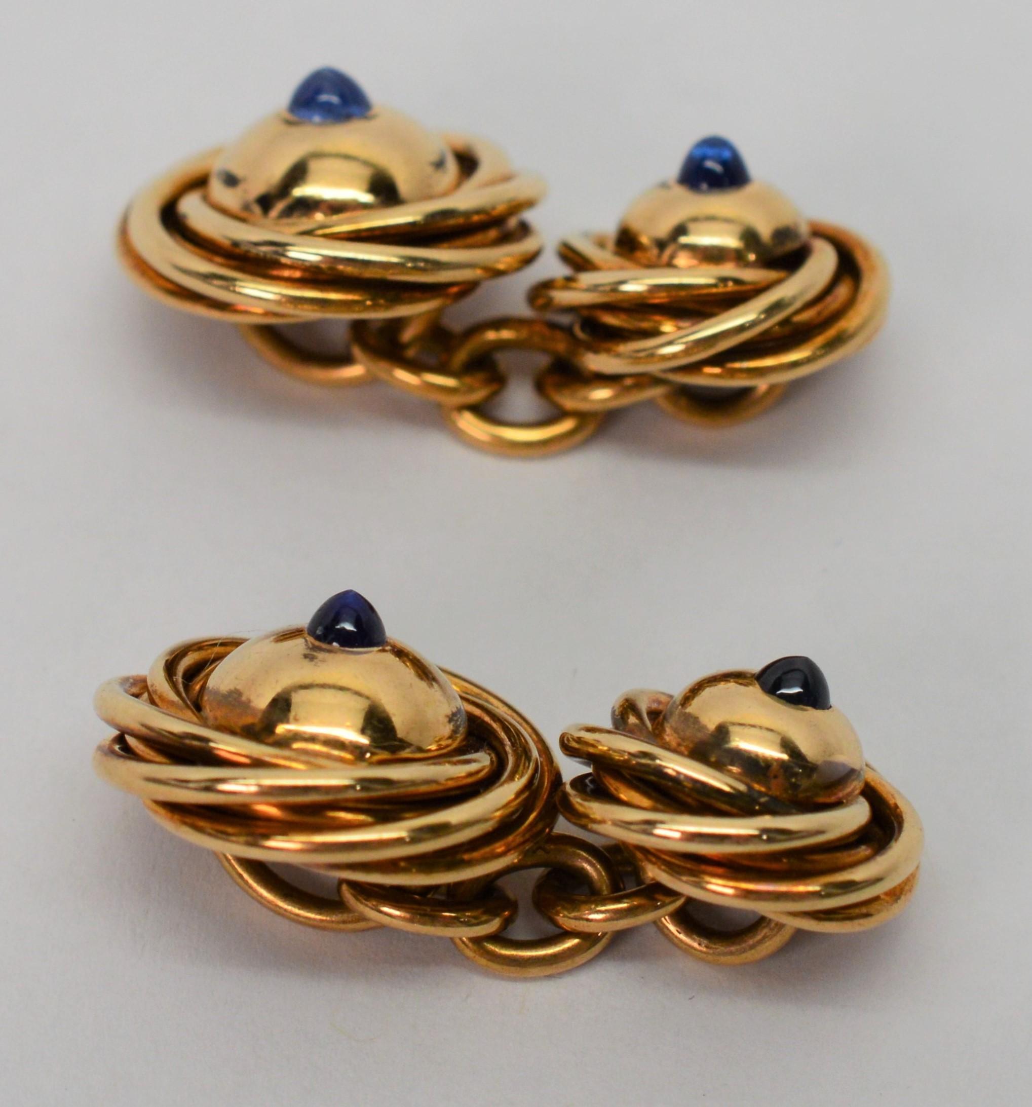 Finer details give that finished look. Enjoy this pair of pre-war fourteen karat 14K yellow gold knot cuff links tastefully appointed with a blue sapphire cabochon gemstone accents. Fitted with chain links, the knot heads measure 12.59mm and 15.27