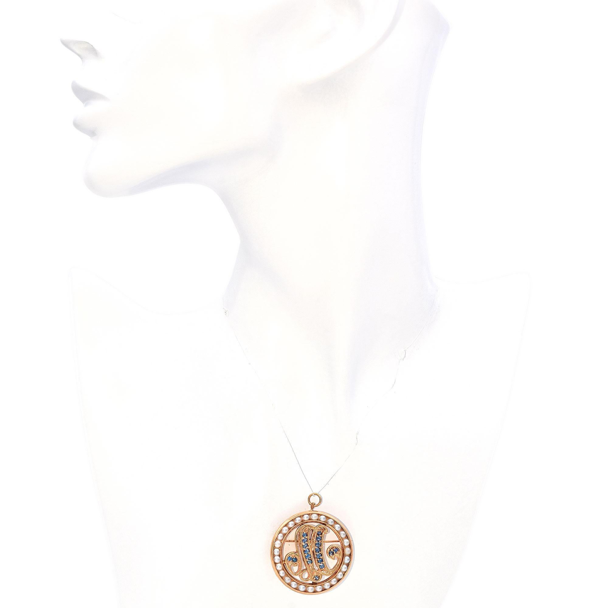 Designed in a circular form this brooch features a central M letter monogram adorned with vibrant blue sapphires. Encircled by a border of lustrous pearls. A hidden bail it attached at the back allowing the piece to be worn as a