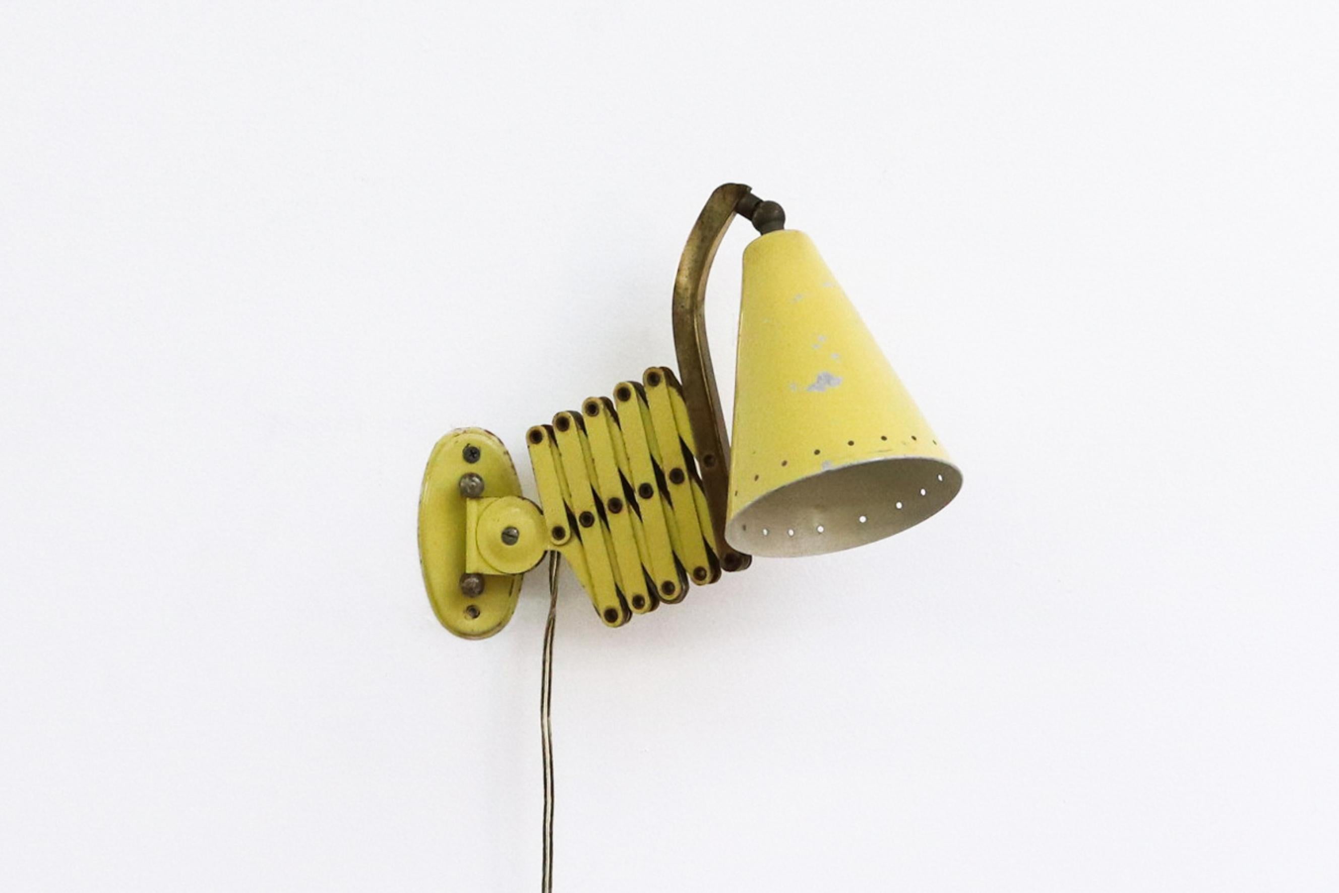 Pale yellow Enameled Hala Zeist scissor arm wall mount lamp with perforated shade and brass hardware. In original condition with visible wear including some enamel loss, Wear is consistent with age and use.