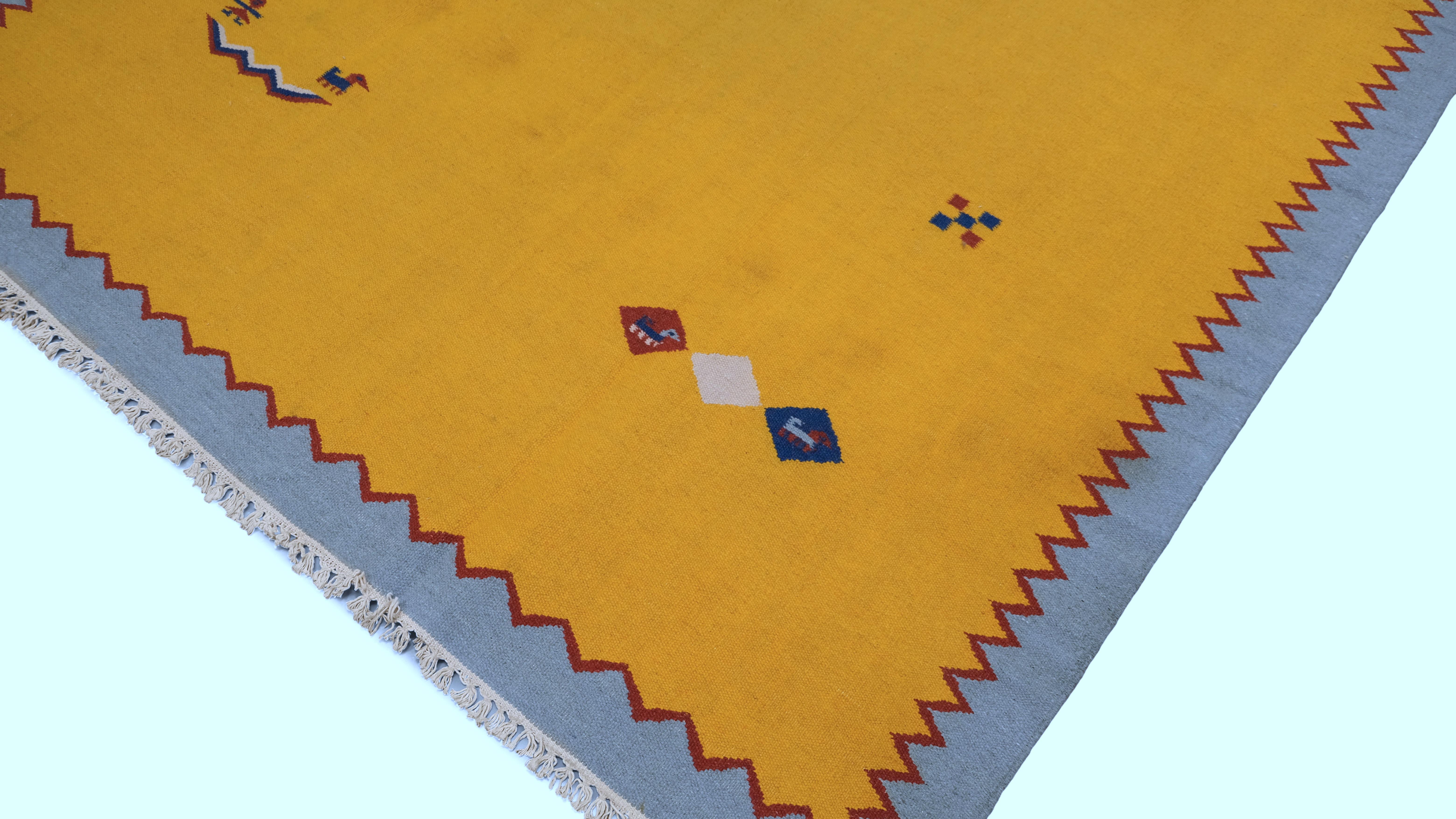 This handwoven wool kilim showcases a vibrant and minimalist tribal aesthetic, blending traditional craftsmanship with a contemporary edge. The bold golden-yellow field is framed by a subtle gray border, accentuated with a zigzag red, white and blue