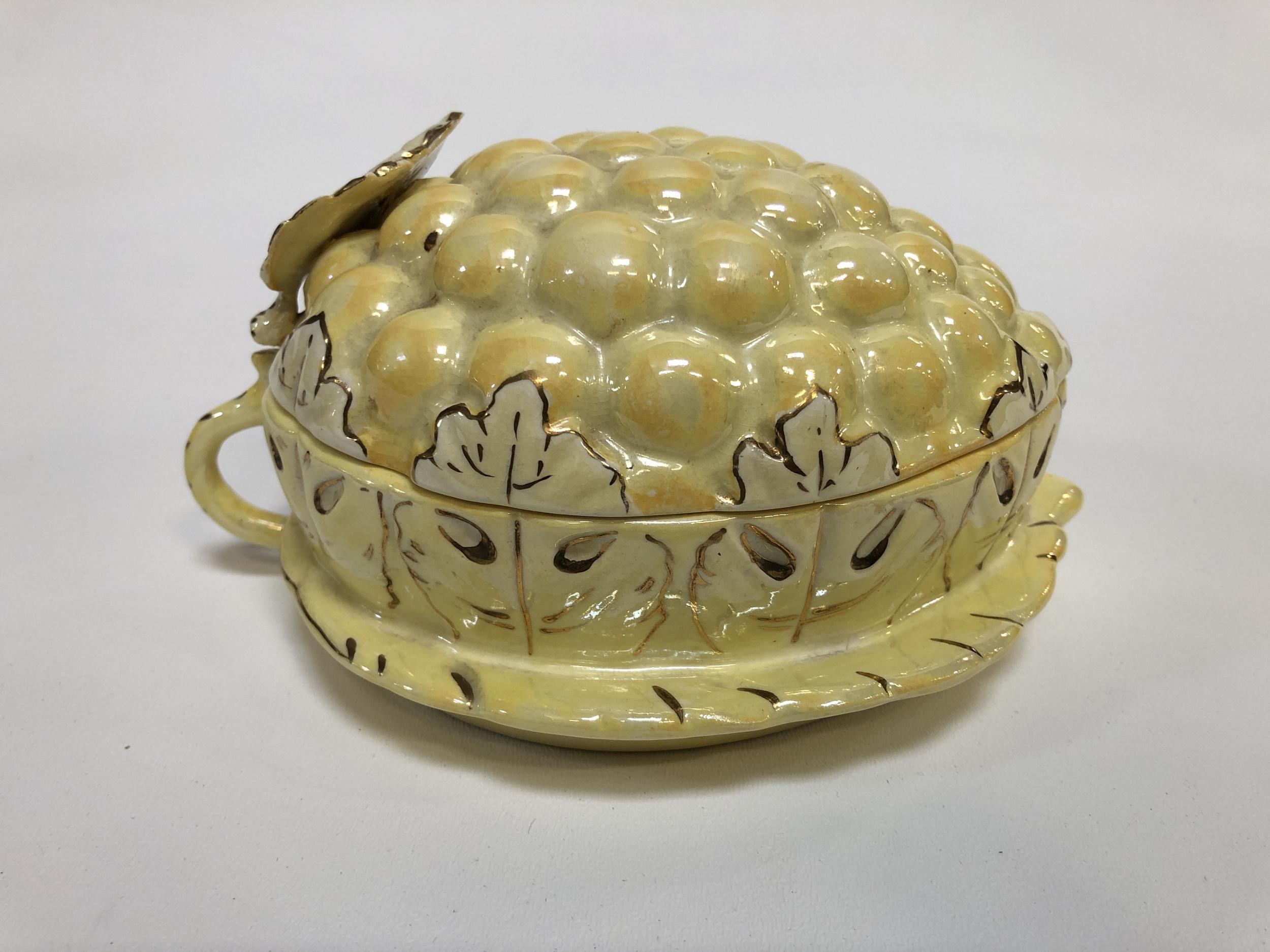 This vintage covered dish is made out of porcelain ceramic. It depicts bright yellow grapes with green-tinted grape leaves, hand-painted with gold veins and finished with a lusterware glaze.

This lusterware grapes box was made by Sasha in the USA