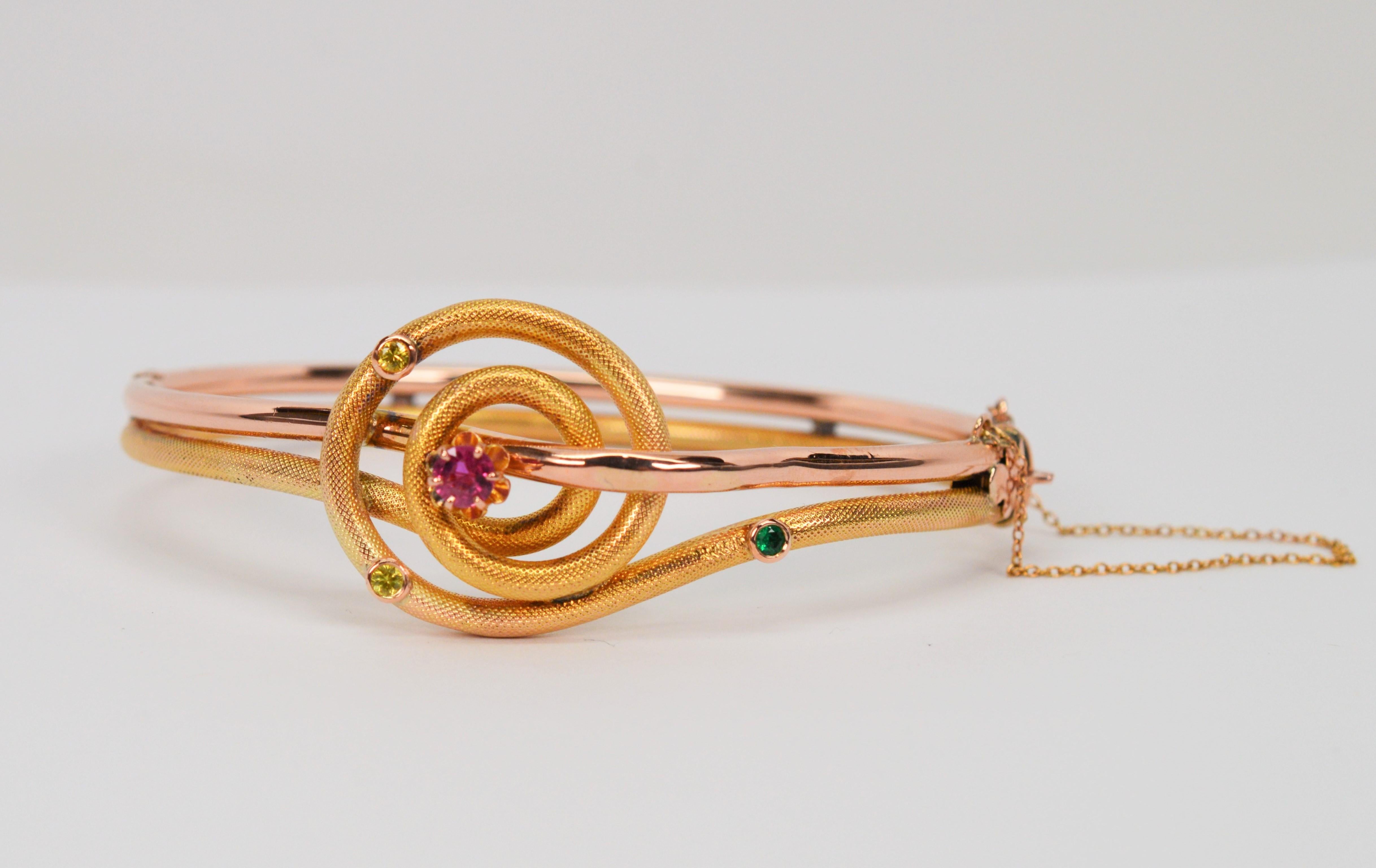 Artful swirls of textured 14 karat yellow gold intertwined with the warmth of rose gold lend a whimsical look to this unique vintage bangle bracelet. Asymmetrically placed colorful gemstone accents including ruby, emerald and yellow sapphire