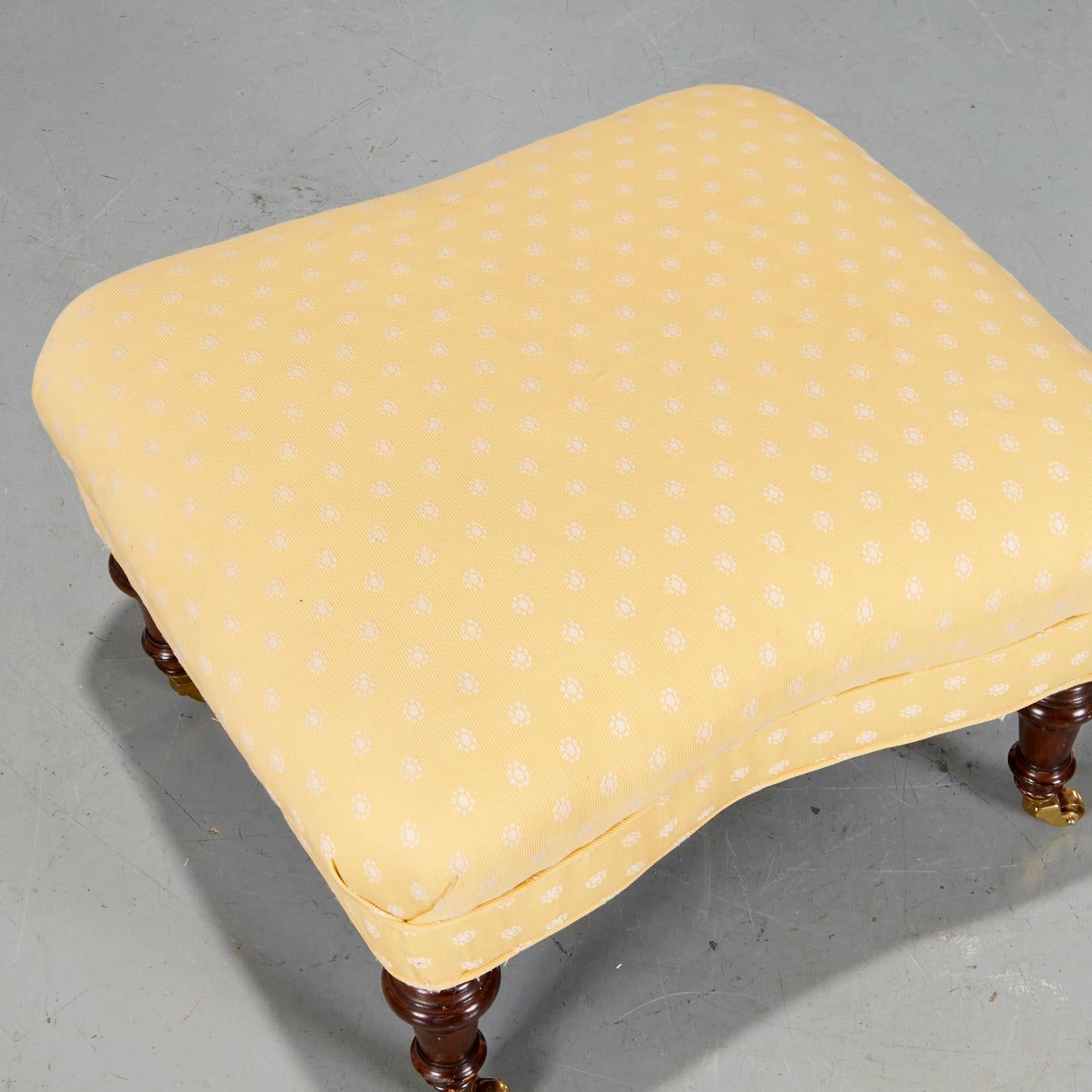 Vintage s. XX, pequeña otomana tapizada en amarillo con delicado estampado floral blanco, sobre patas torneadas de caoba, terminadas en ruedecillas, sin marcar, 

Las patas de madera maciza con detalles torneados están equipadas con ruedas de latón