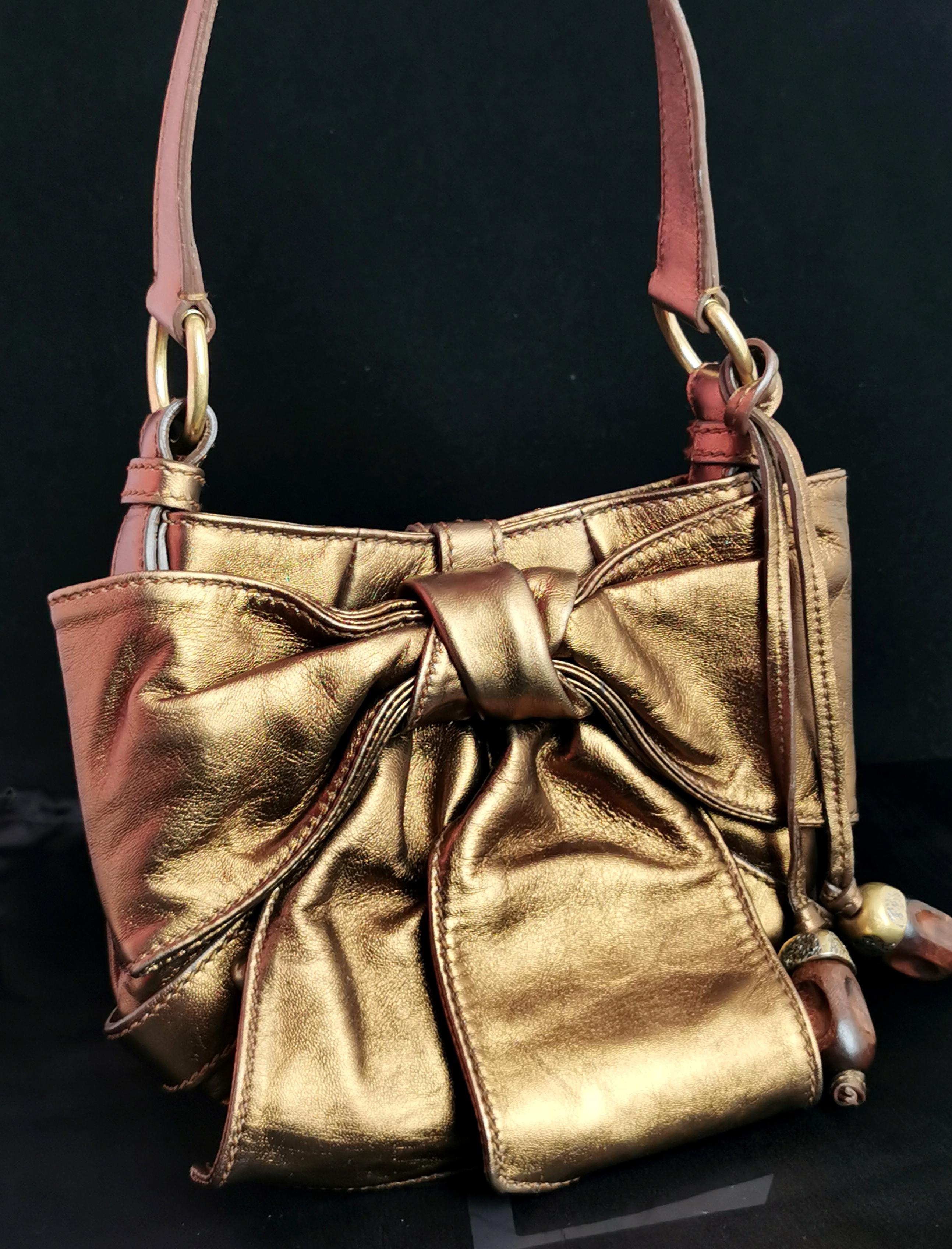 A gorgeous vintage YSL bronze bow mini bag.

A lovely super soft warm bronze tone lambskin leather with a bow front and gold tone and wood hardware.

It has acorn shaped tassle and closes with a large press stud fastener.

It has a large bow to the