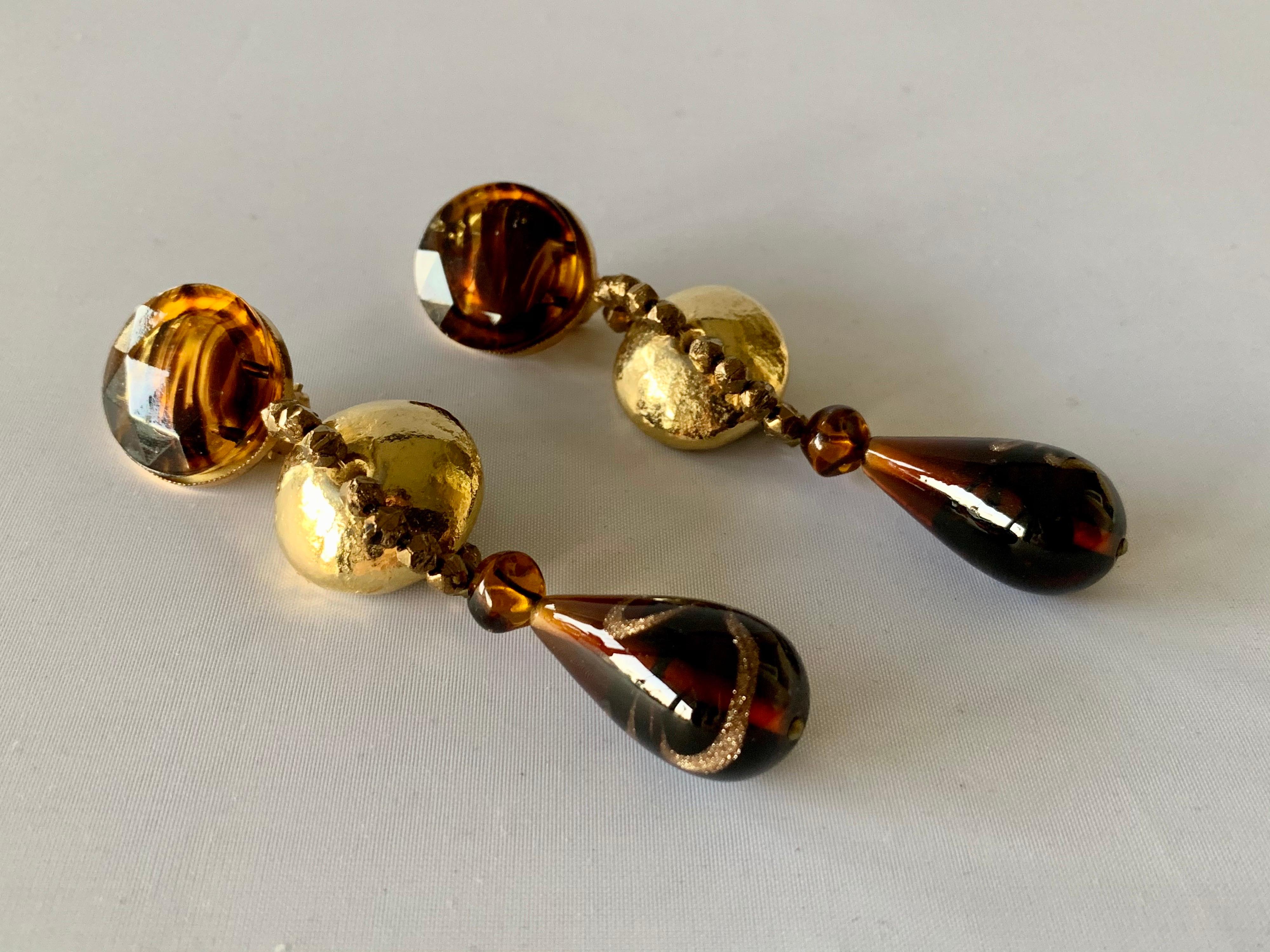 Exceptional vintage YSL chandelier statement clip-on earrings featuring a bold design - comprised out of light-brown glass segments with metallic gold details, faceted bronze beads, and large metallic gold disks at the center. The earrings are