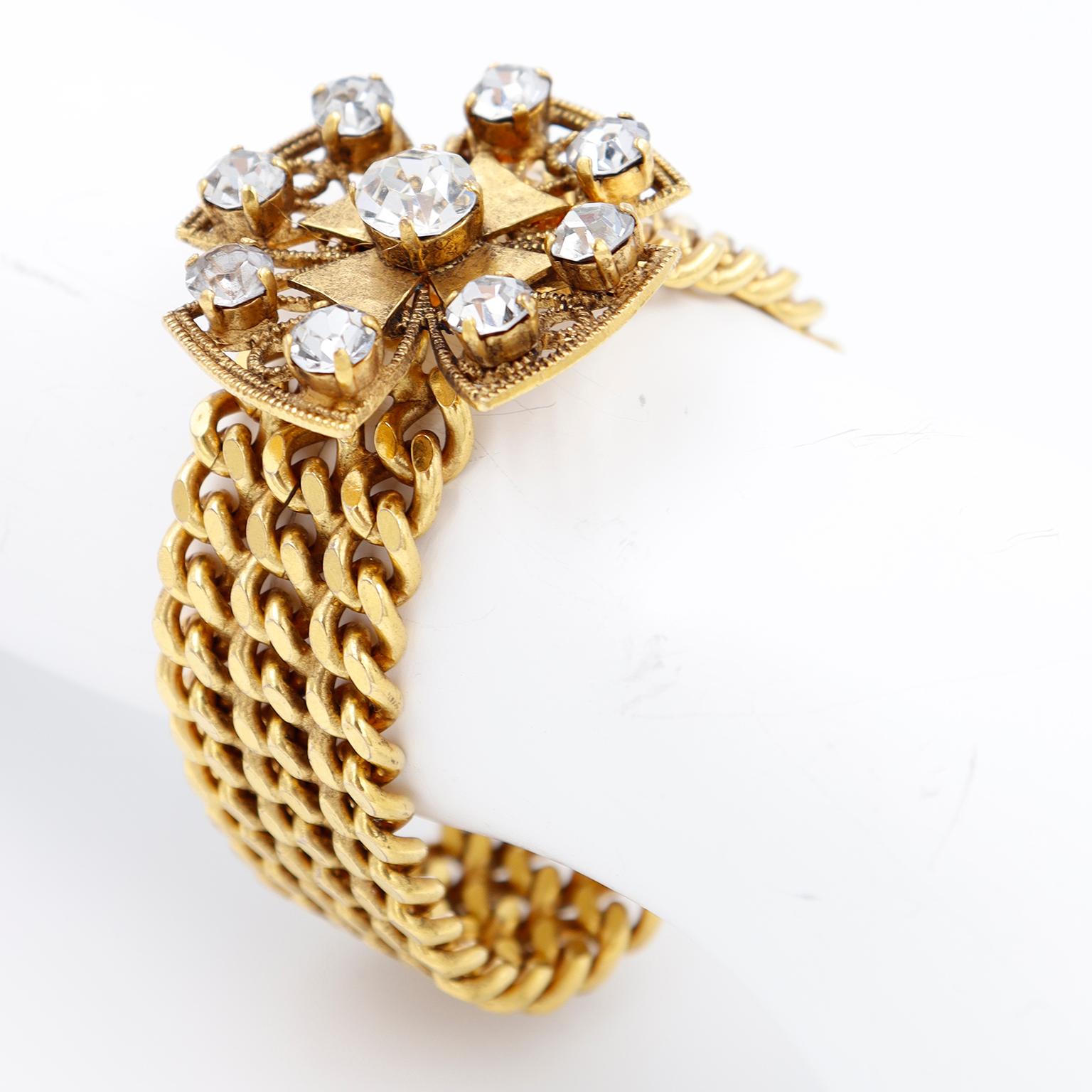 This unique vintage Yves Saint Laurent bracelet is comprised of a triple row of gold plated curb chains that close with a branded YSL hook under a maltese cross embellished with faceted rhinestones. This bracelet is comfortable to wear and is