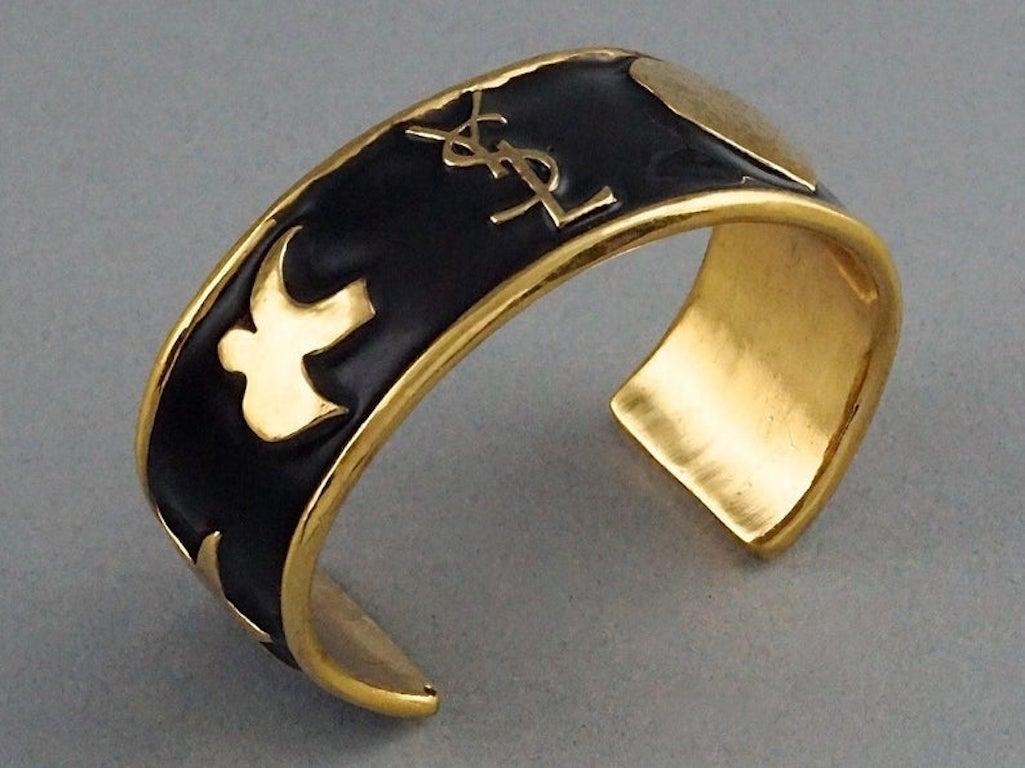 Vintage YSL Yves Saint Laurent Iconic Logo Emblem Enamel Bracelet Cuff

Measurements:
Height: 1 inch (2.5 cm)
Circumference: 6.02 inches (15.3 cm)

Features:
- 100% Authentic YVES SAINT LAURENT.
- Black enamel cuff bracelet.
- Raised YSL logo and