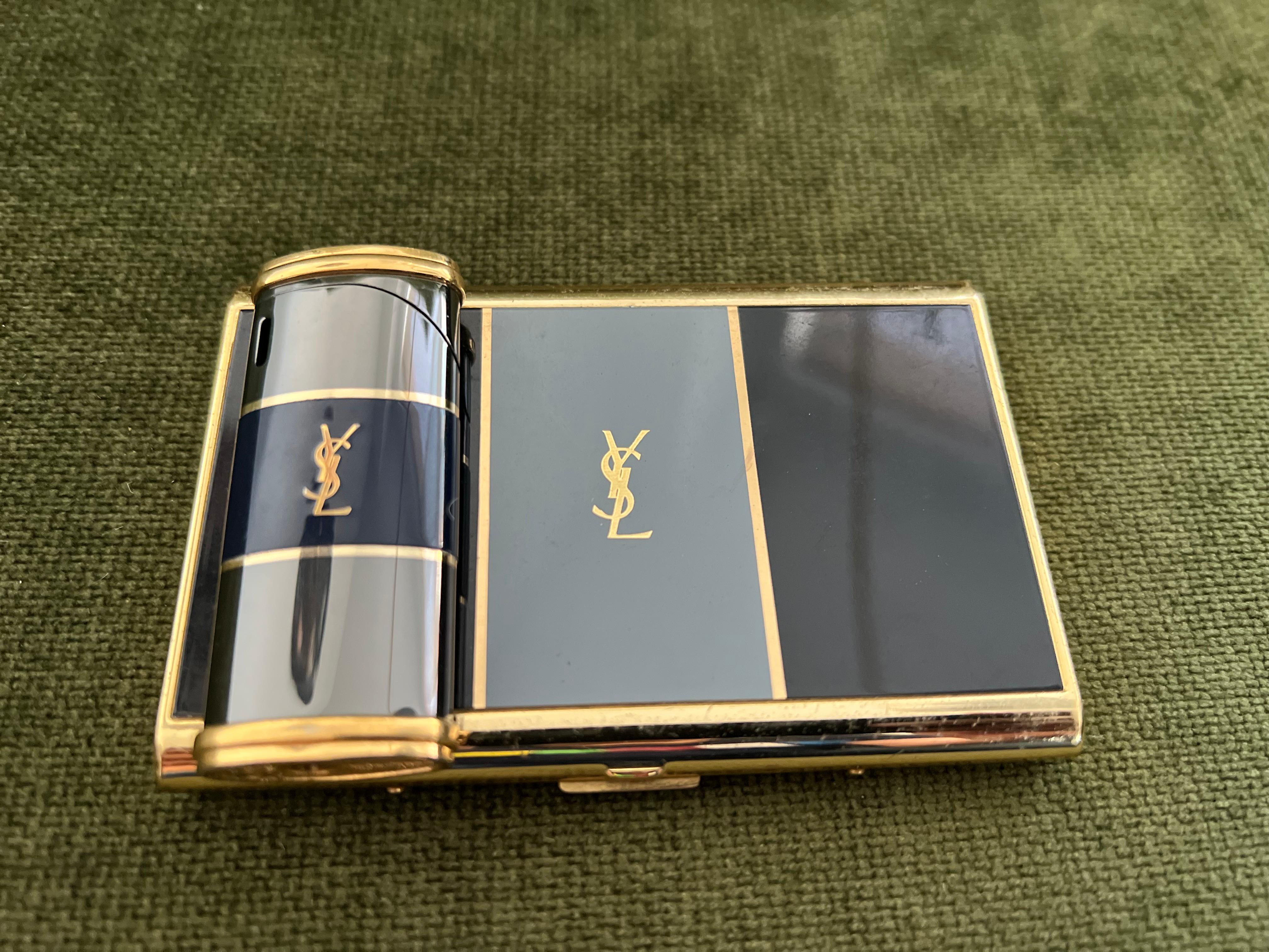Vintage “YSL” Yves Saint Laurent Retro Cigarette Case & Lighter Set 
“Circa 1980”
“YSL” Yves Saint Laurent retro cigarette case and lighter 
Logo Cigarette Case Gold Black Blue
The case is in mint condition. It has never been used. 
The clasp snaps