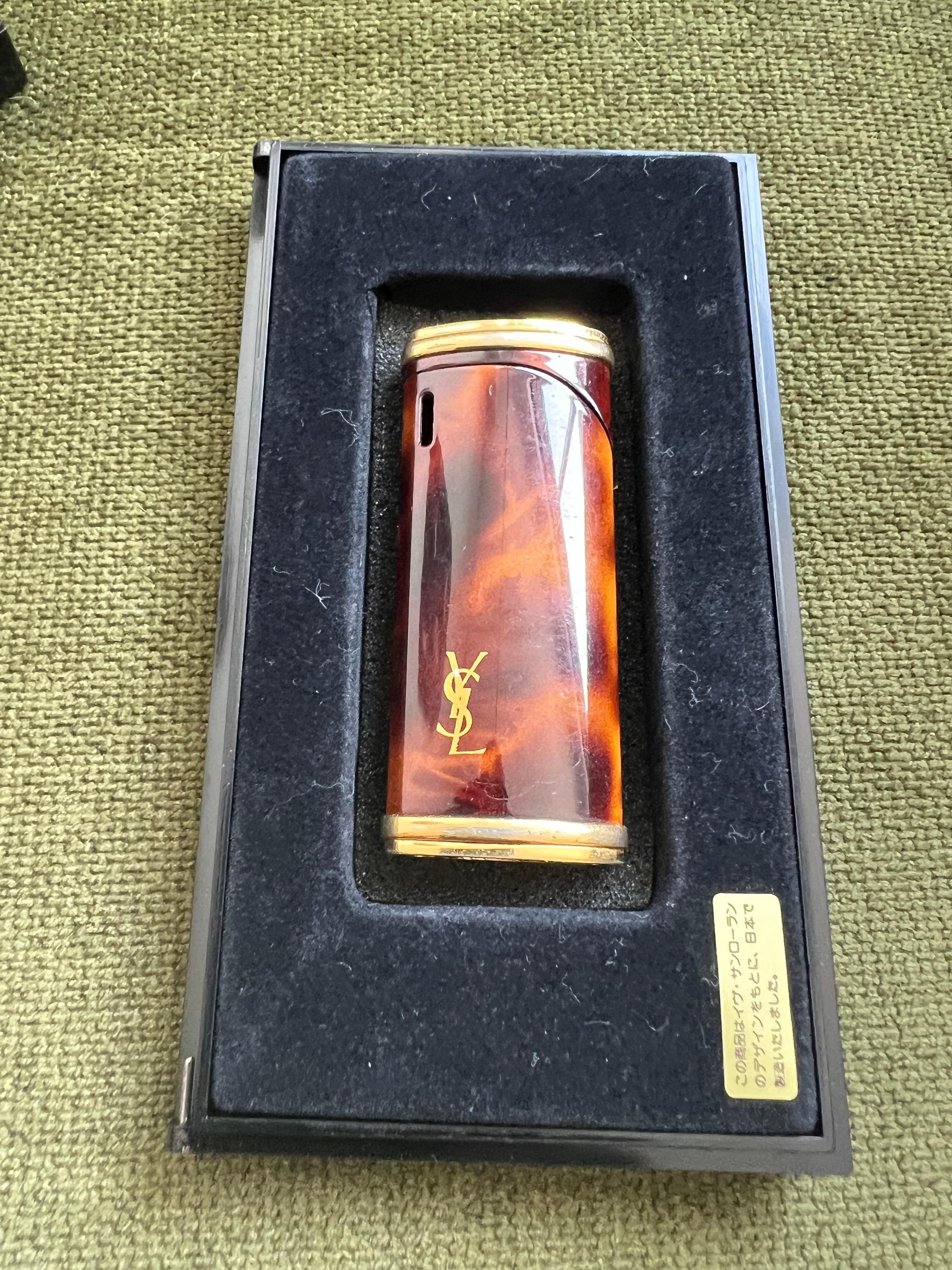 Rare Cognac & Gold Vintage “YSL” Yves Saint Laurent Retro Cigarette Lighter, Circa 1980s Original Case
“YSL” Yves Saint Laurent retro cigarette lighter 
Logo 
Cognac and Gold 
The Lighter  is in mint condition. Was never used.
In original Yves Saint