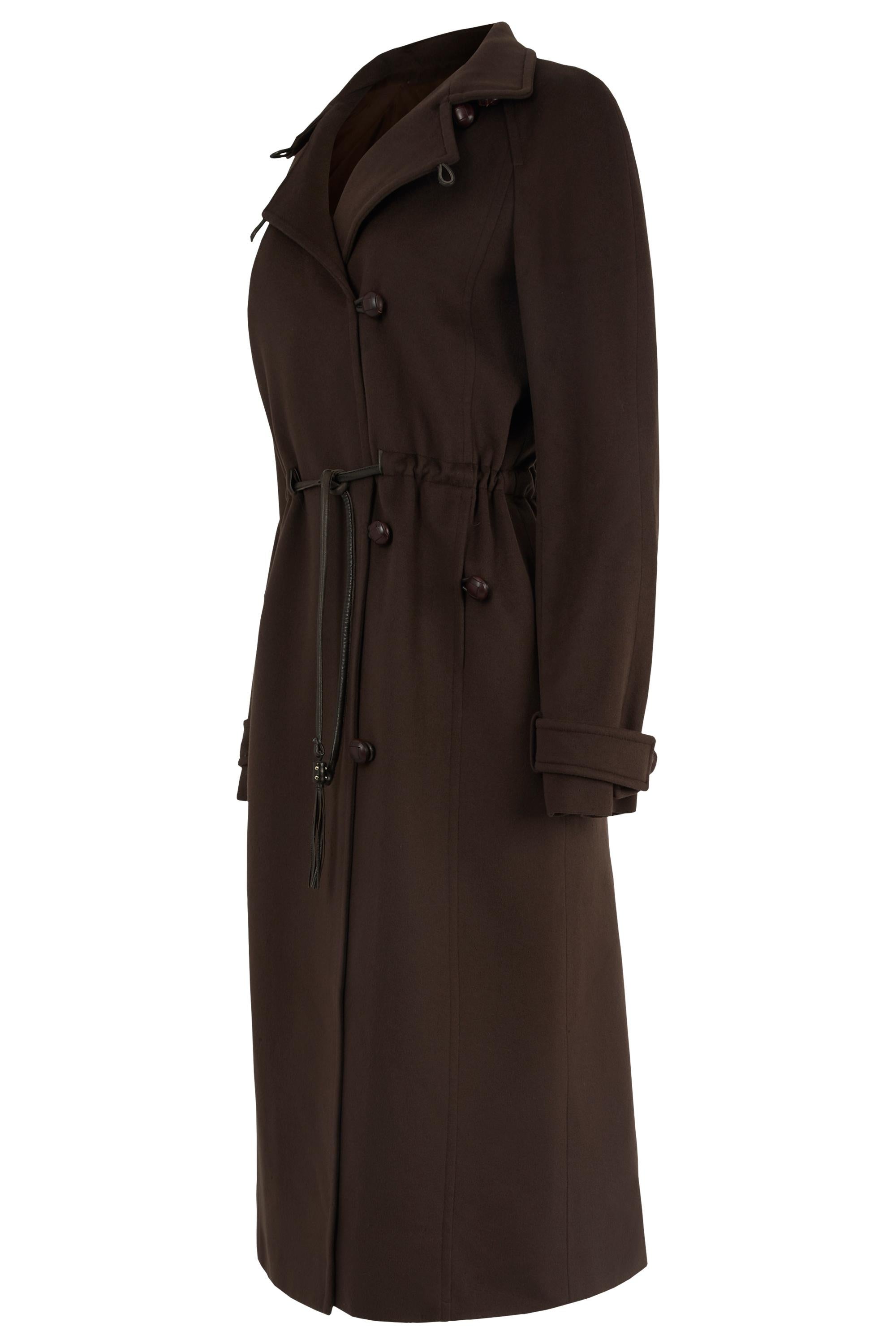 Colección Vintage Yves Saint Laurent Otoño/Invierno 2004, Presenta un lujoso tejido de lana marrón, un escultural cuello alto, un cierre de botones asimétrico y una cintura ceñida acentuada con un lazo de cordón de piel Acabado con puños con