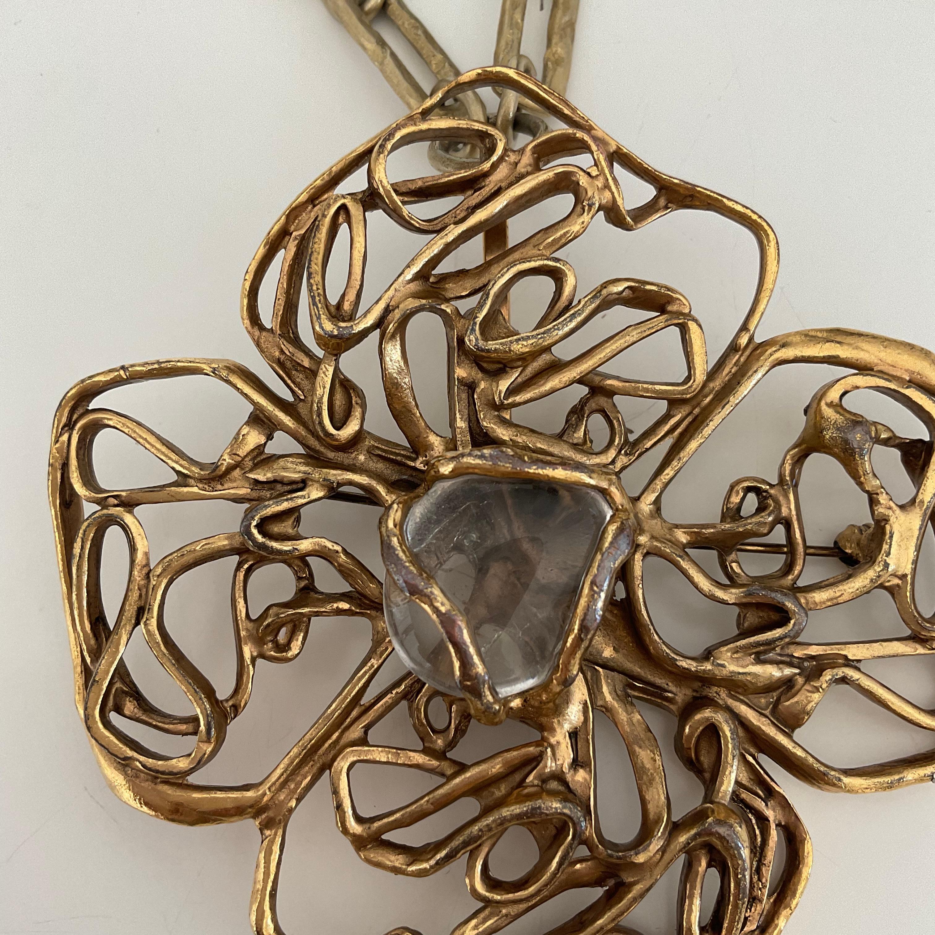 This original and one-of-a-kind brooch is a vintage piece from Yves Saint Laurent from the 70's. Gold-toned, it is designed as a flower, composed of four petals with wired chains/links, with a clear rock crystal at the centre. The brooch becomes a