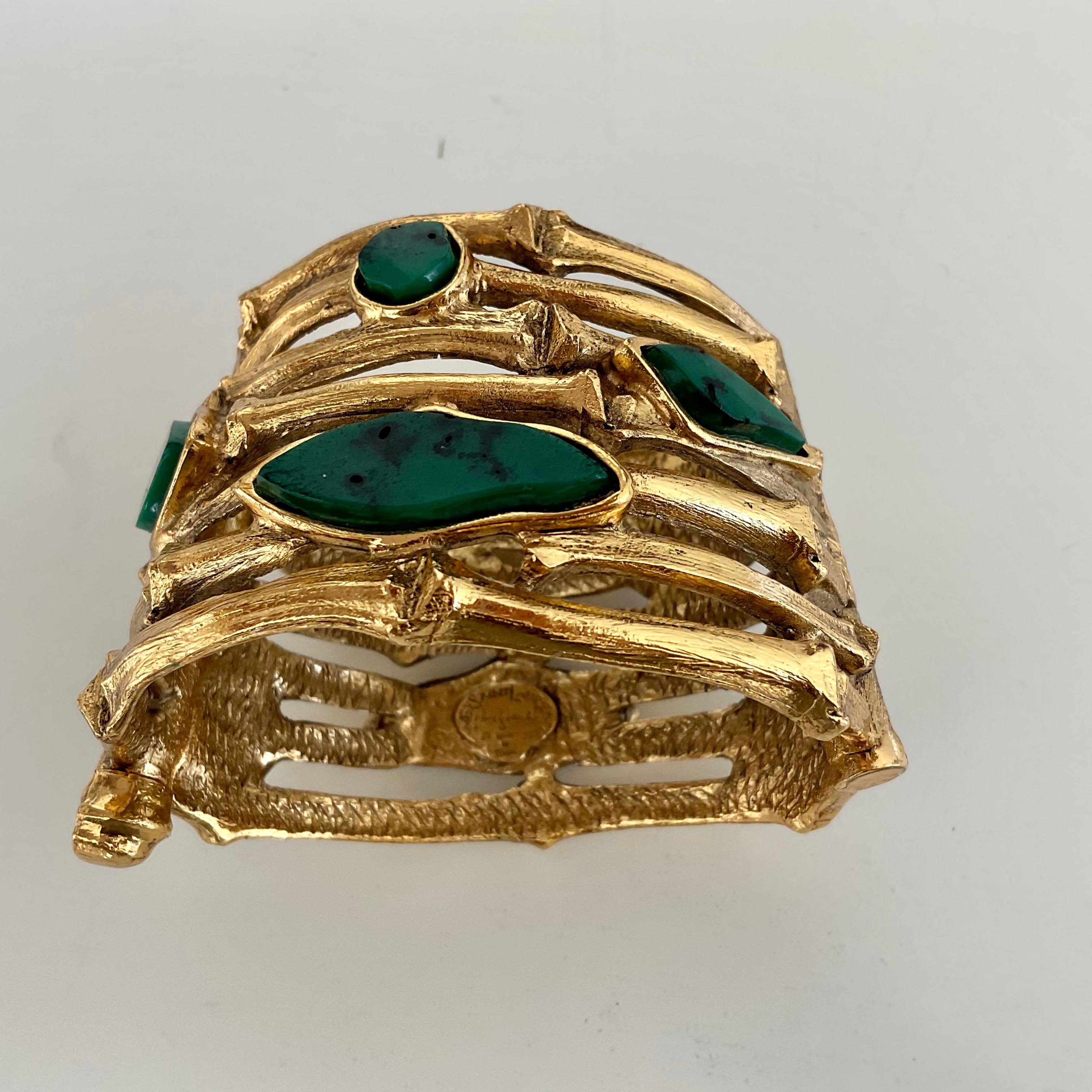 Ce bracelet unique d'Yves Saint Laurent, datant des années 70, est un bracelet manchette plaqué or. Conçues comme des branches de bambou, elles sont composées de pierres en résine de différentes formes, d'aspect naturel, de couleur verte à noire. A