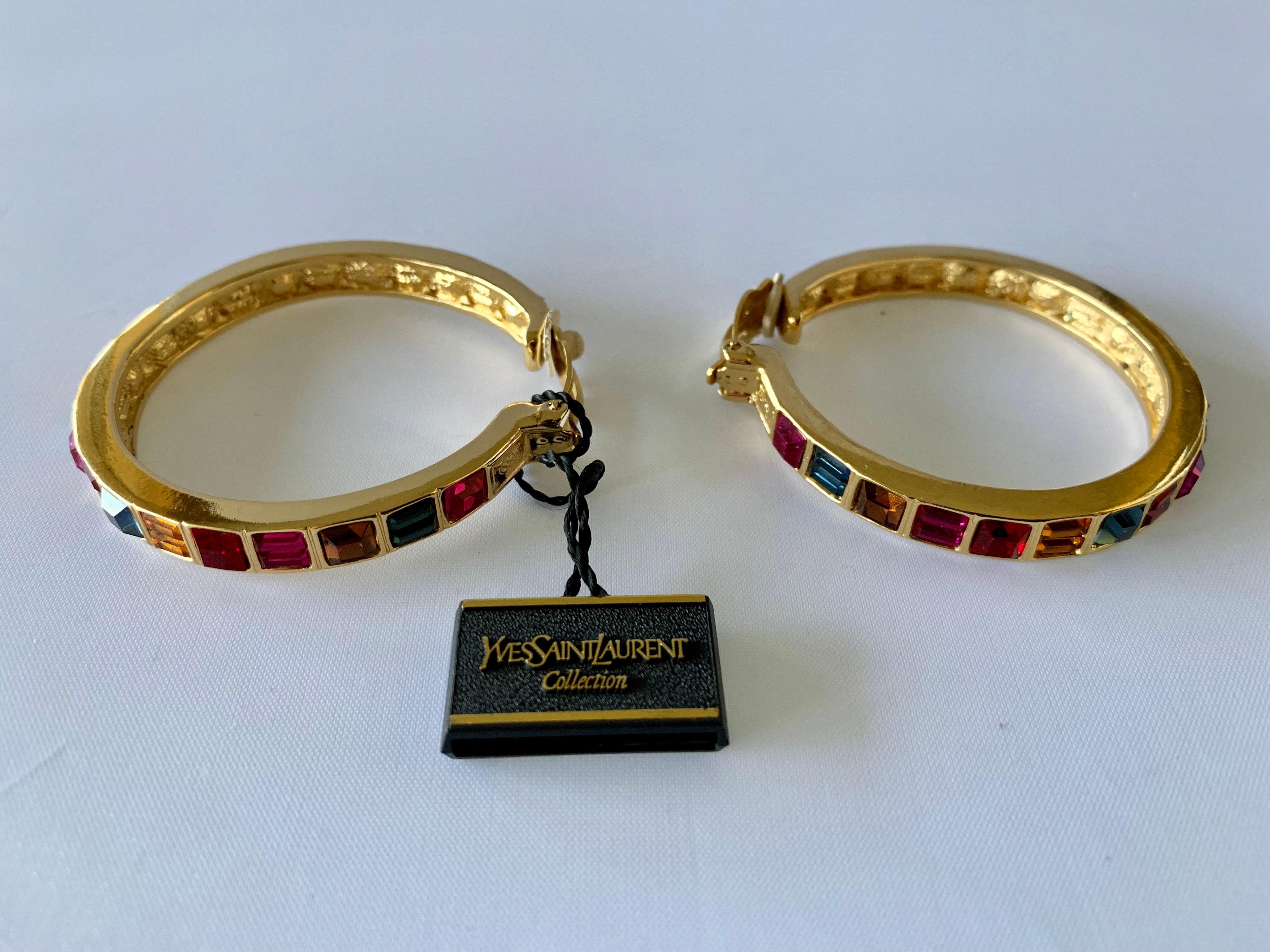Vintage Yves Saint Laurent jeweled gold hoop statement clip-on earrings by Robert Goossens. The hoop earrings are comprised out of gold-tone metal in a sleek contemporary manner and are adorned by channel-set glass stones in red, fuchsia, blue, pink