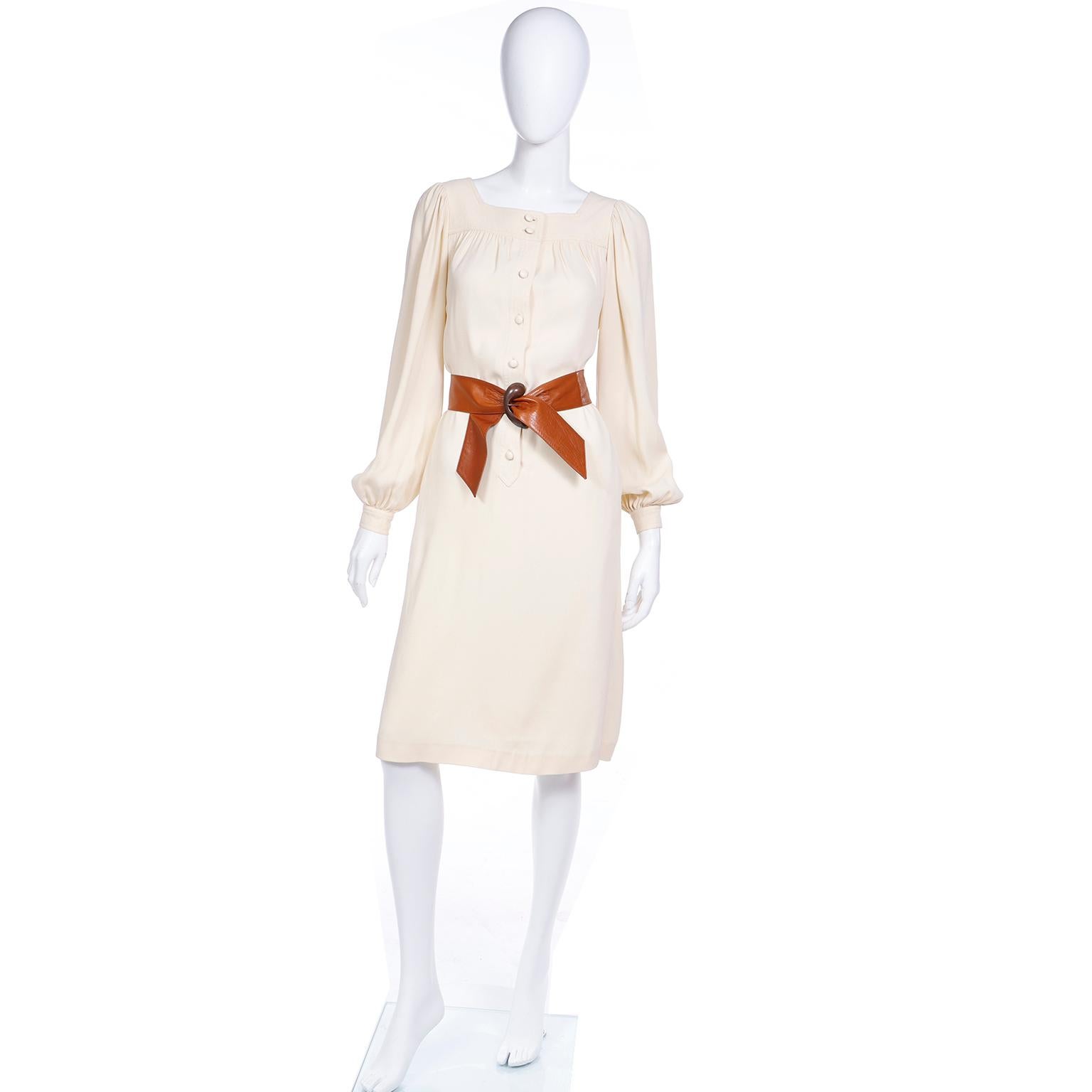 This is a classic example of a late 1970's Yves Saint Laurent smock dress, in a neutral light beige jersey fabric and featuring bishop-style sleeves. The dress bears the YSL signature pleating at the yoke and is embellished with round cream plastic