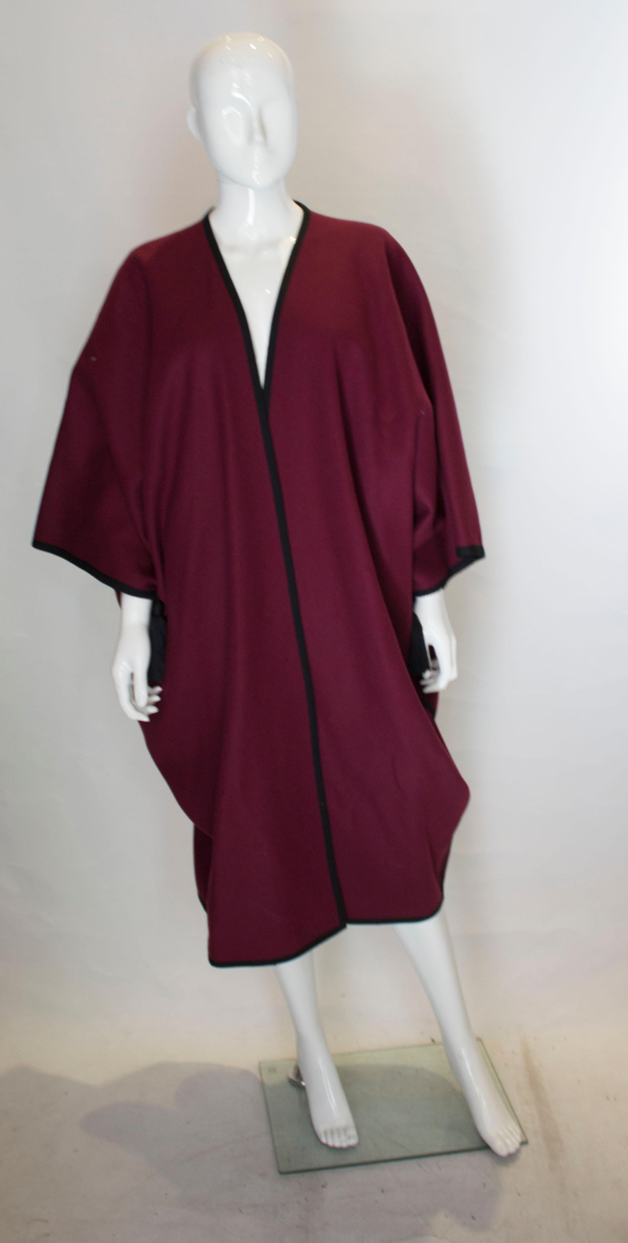 A great addition for Fall from Yves Saint Laurent Rive Gauche . This cape is in burgundy wool with a black trim , and black silk tassles on each arm.