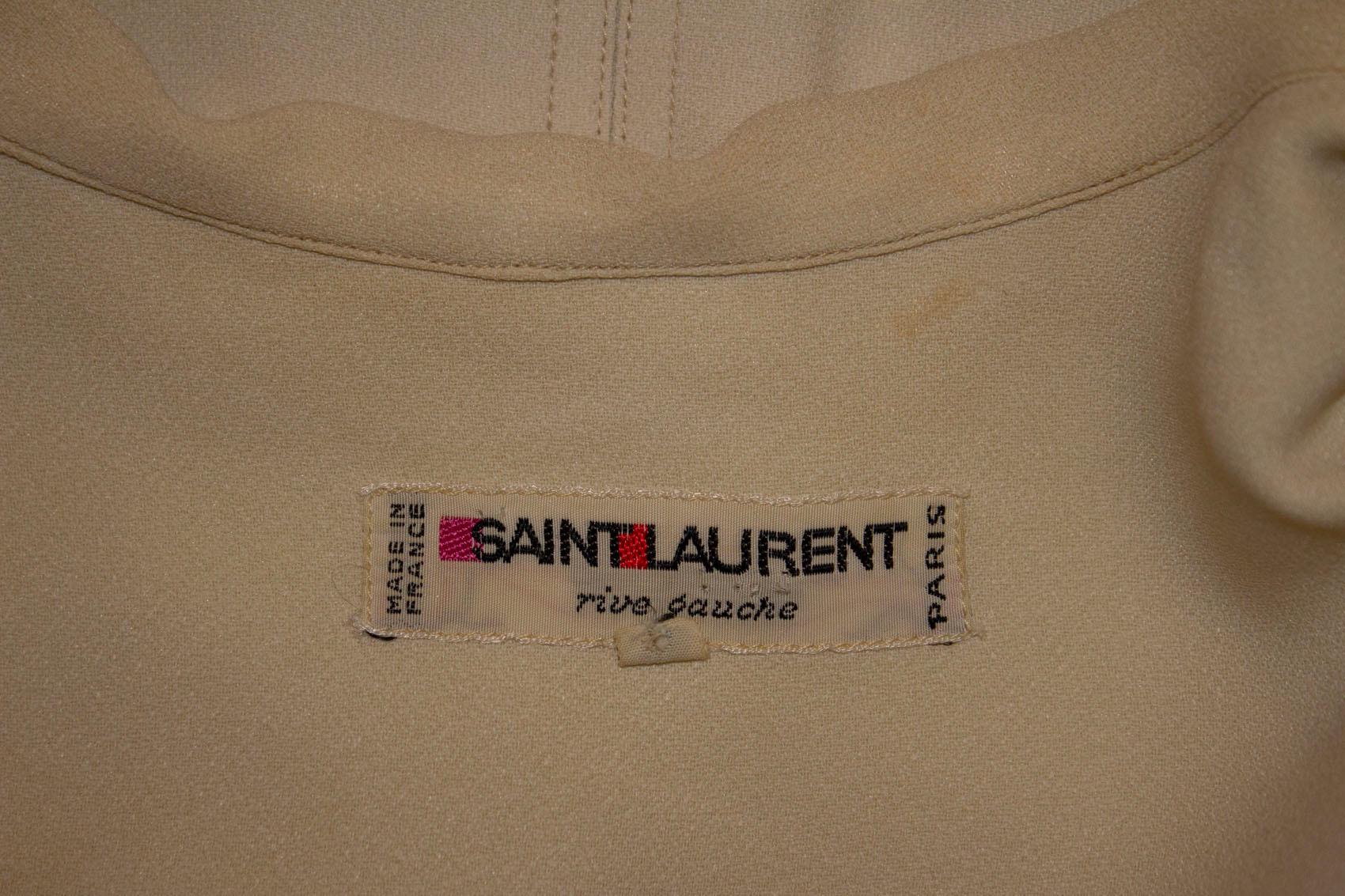 A chic vintage day dress by Yves Saint Laurent , Rive Gauche . In an ivory crepe , the dress has a button down opening at the front , and sewn in pleats from the waist producing a neat line. It went to a good party , and sadly has a cigarette burn