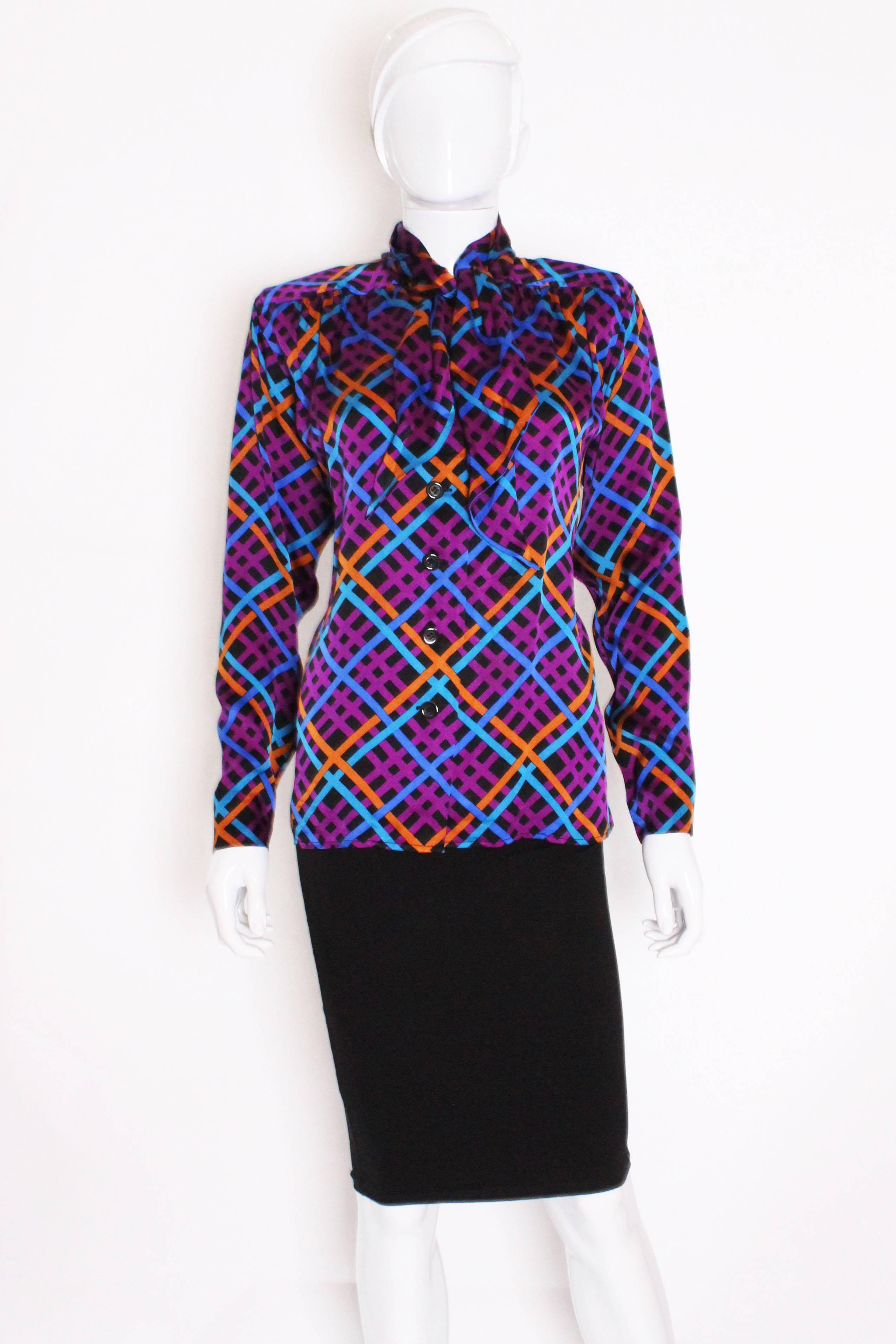 A stunning blouse from Yves Saint Laurent Rive Gauche. As you would expect the silk is of a superior quality and the colours are bold. The blouse has a black background, with orange, purple, blue and turquoise lines running across.There is gathering