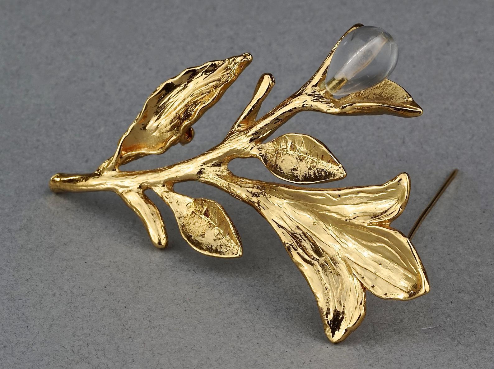 Vintage YVES SAINT LAURENT Ysl Glass Flower Stem Brooch

Measurements:
Height: 3.07 inches (7.8cm)
Width: 2.04 inches (5.2 cm)

Features:
- 100% Authentic YVES SAINT LAURENT.
- Textured flower stem brooch.
- Clear glass flower bud accent.
- Gold